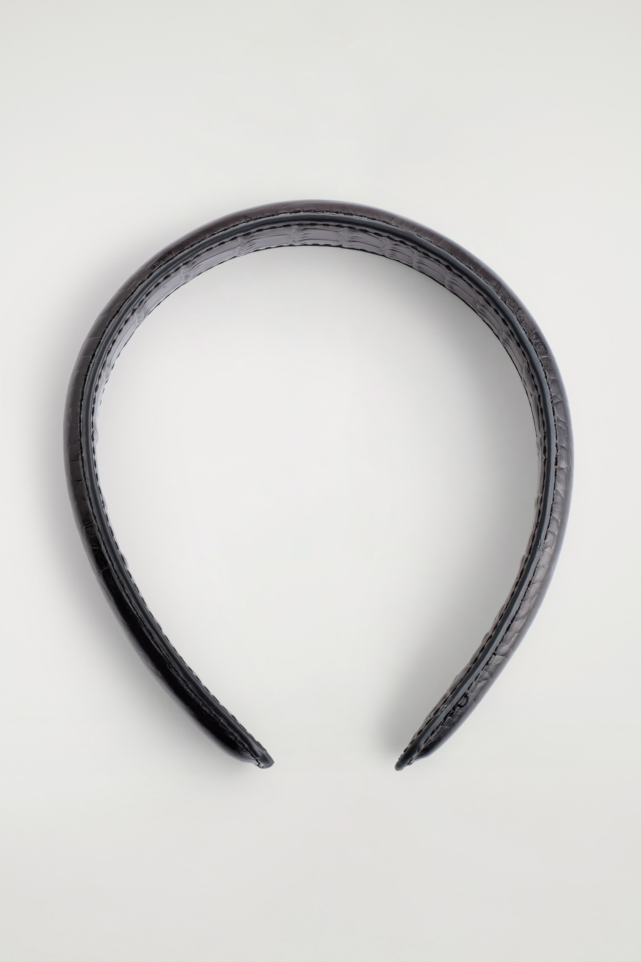 Ver imagen más grande: Una diadema de cuero marrón oscuro está colocada plana en una vista SUPERIOR, con un distintivo estampado en relieve con efecto de cocodrilo a lo largo de su superficie curva.