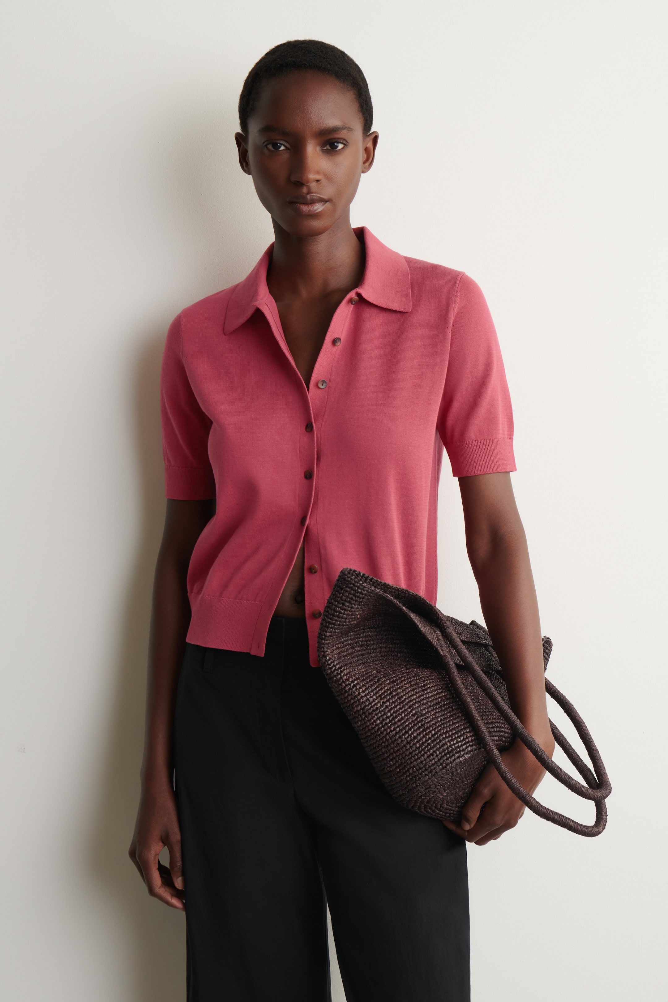 Visualizza immagine più grande: Un cardigan rosa tenue a maniche corte in maglia, caratterizzato da un colletto polo, una chiusura con bottoni marroni e polsini e orlo a coste, presenta una vestibilità rilassata.