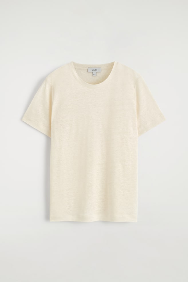 Ein hellcremefarbenes, dezent strukturiertes Leinen-T-Shirt zeigt seine Vorderseite. Es verfügt über einen klassischen Rundhalsausschnitt und kurze Ärmel. - 1
