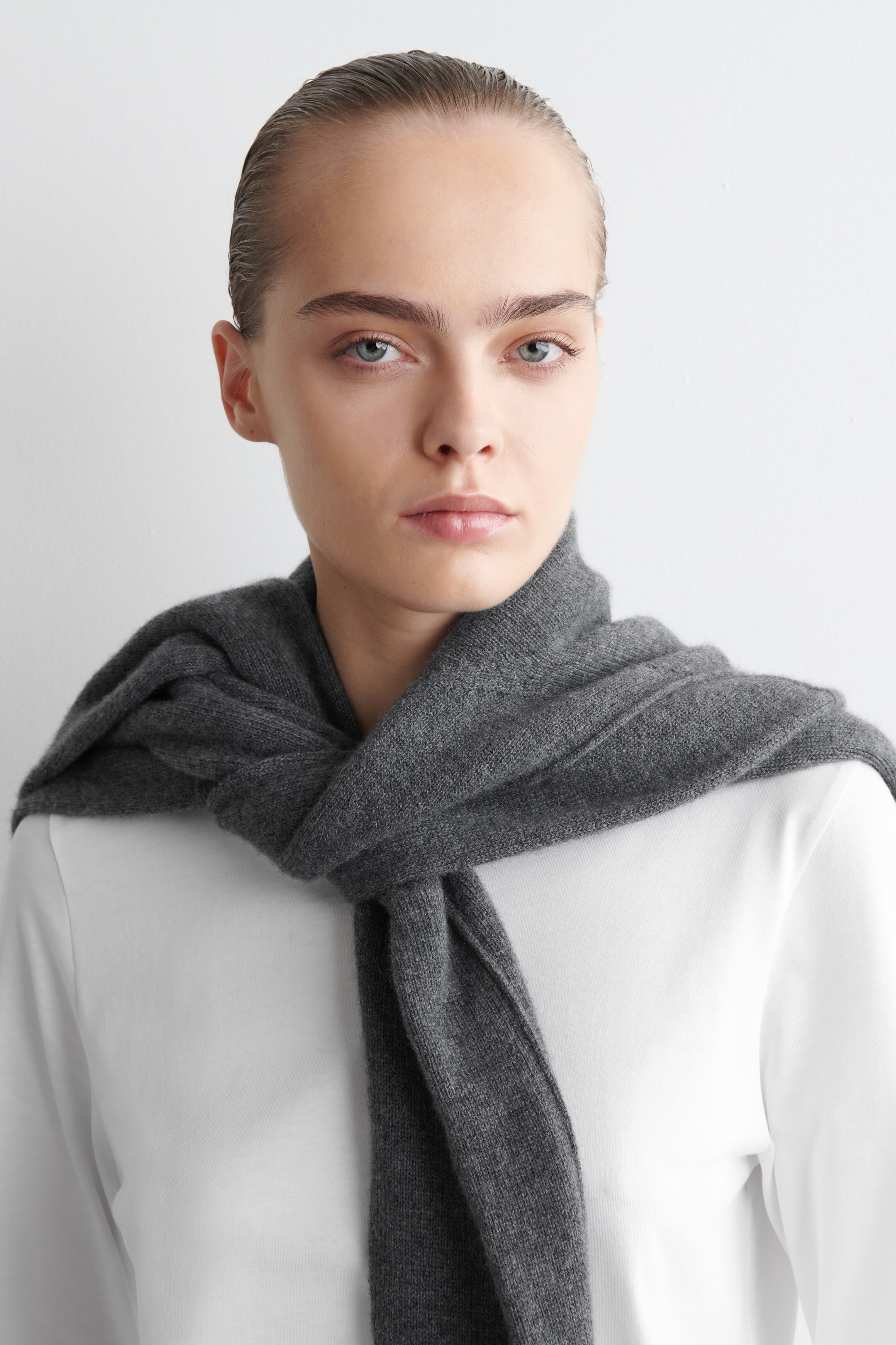 Agrandir l'image: Un haut blanc à manches longues est porté, présenté sous l'angle du TOP. Il présente un col rond, partiellement visible sous une écharpe en tricot gris foncé qui est enroulée et nouée autour du cou.