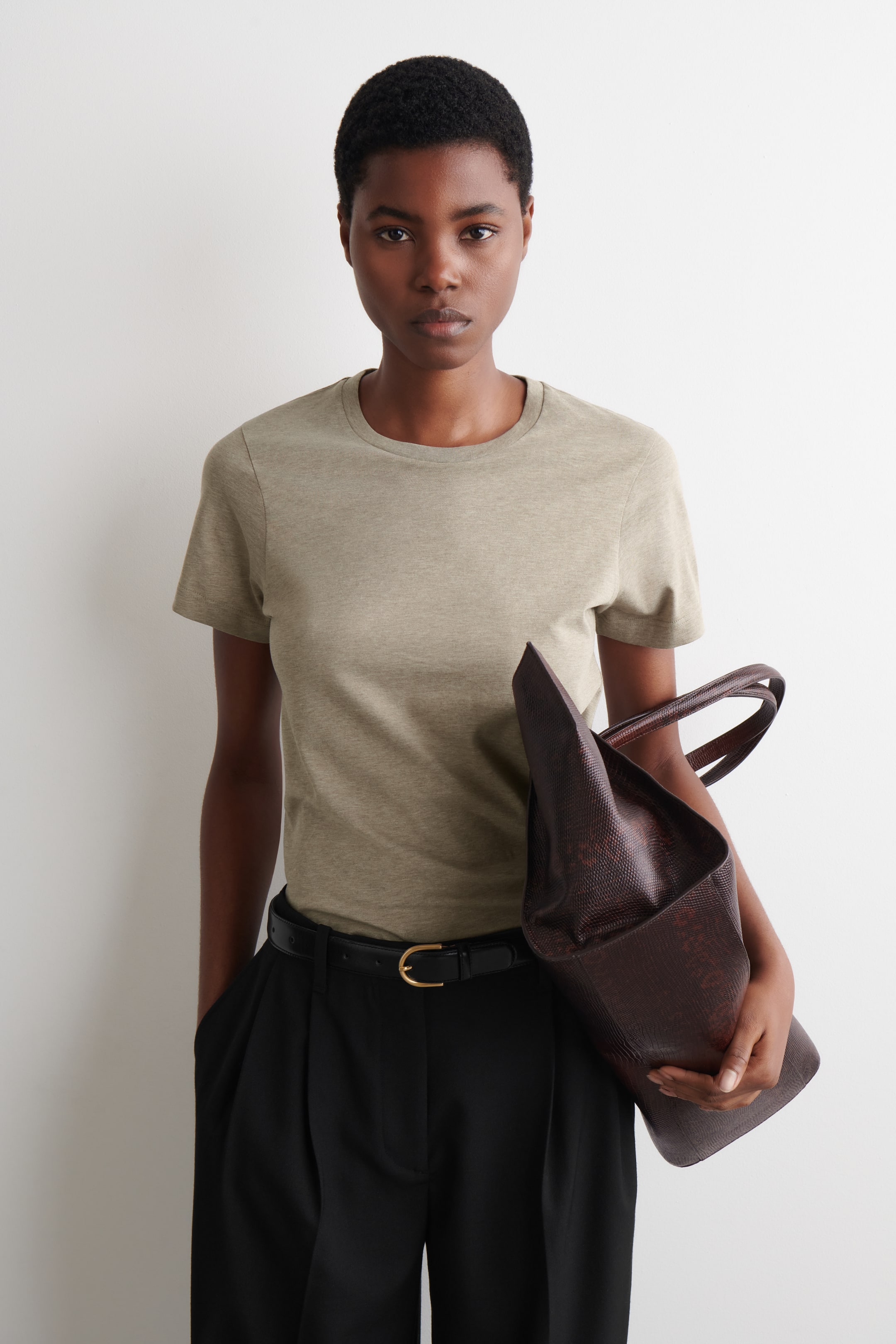 Grotere afbeelding bekijken: Een licht olijfgroen t-shirt met een ronde hals, korte mouwen en een klassieke pasvorm, momenteel ingestopt in een zwarte broek.