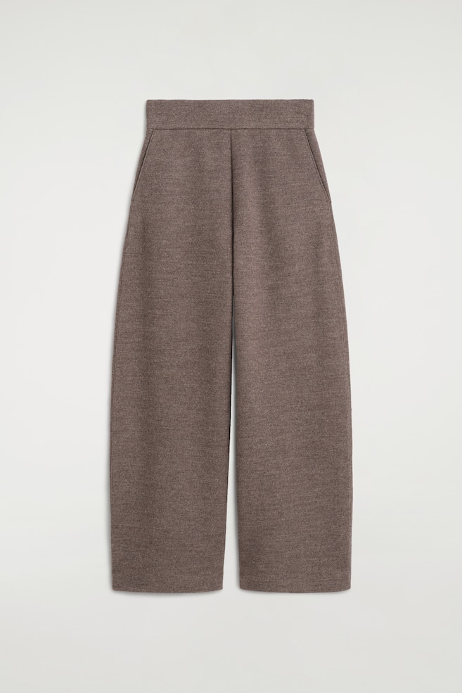 Estos pantalones de pernera barrel de mezcla de lana hervida se muestran de frente, con un punto texturizado en marrón jaspeado y una cintura alta y estructurada. El diseño presenta una silueta ancha y curvada que se estrecha ligeramente en el bajo, con discretos bolsillos laterales insertados en las costuras. - 1