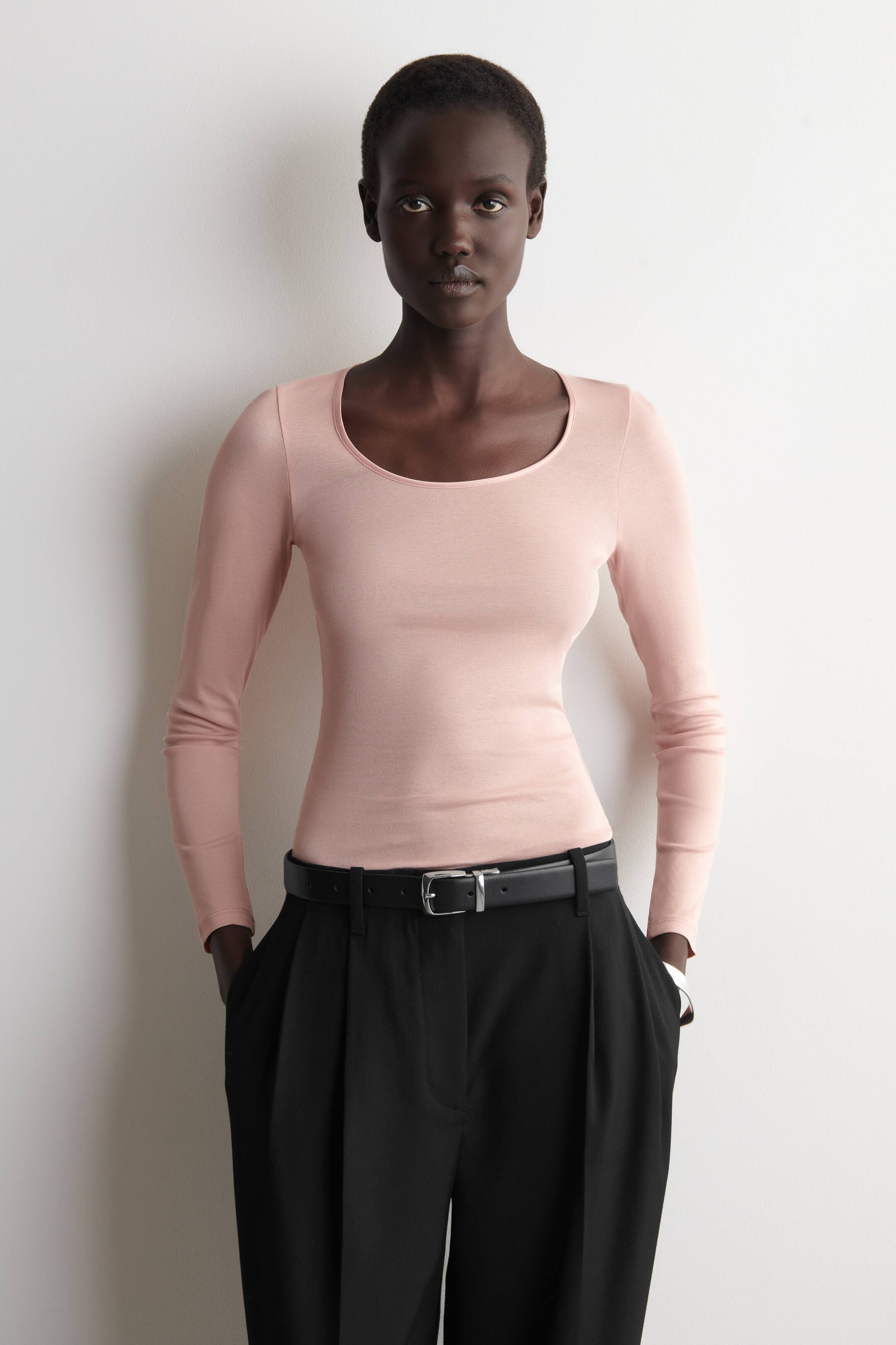 Agrandir l'image: Un haut à manches longues rose clair avec un décolleté arrondi et une silhouette ajustée. Il est présenté rentré dans un pantalon noir.