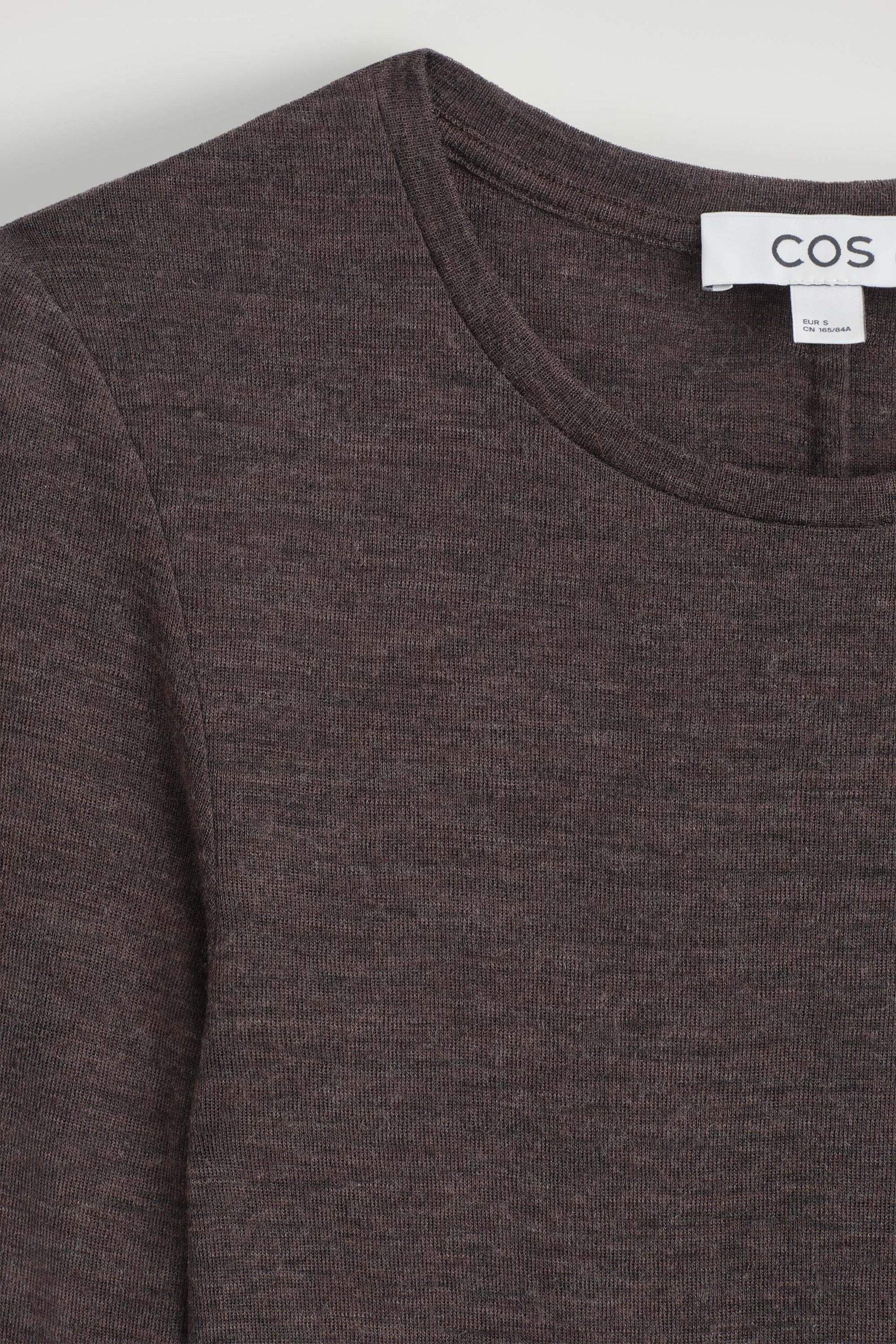 The slim merino wool top is facing front, showcasing its fine-knit, dark brown melange texture. The close-up highlights the round crew neckline with a narrow ribbed trim and the brand label on the inside collar. The slim merino wool top is facing front, showcasing its fine-knit, dark brown melange texture. The close-up highlights the round crew neckline with a narrow ribbed trim and the brand label on the inside collar.