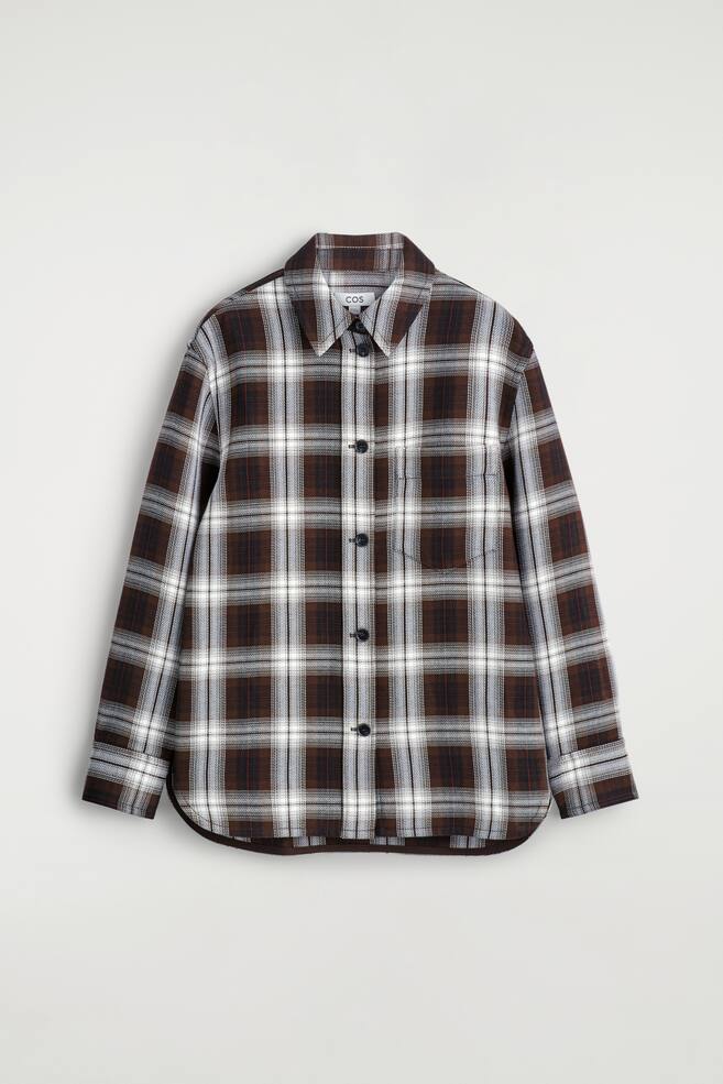 Ein locker sitzendes Overshirt wird VORNE präsentiert, mit einem braun-, weiß- und graukarierten Muster mit dünnen roten Linien. Es ist mit einem spitzen Kragen, einem Knopfverschluss mit dunklen Knöpfen, langen Ärmeln mit Knopfmanschetten, einer einzelnen Brusttasche und einem abgerundeten Saum gestaltet. - 1