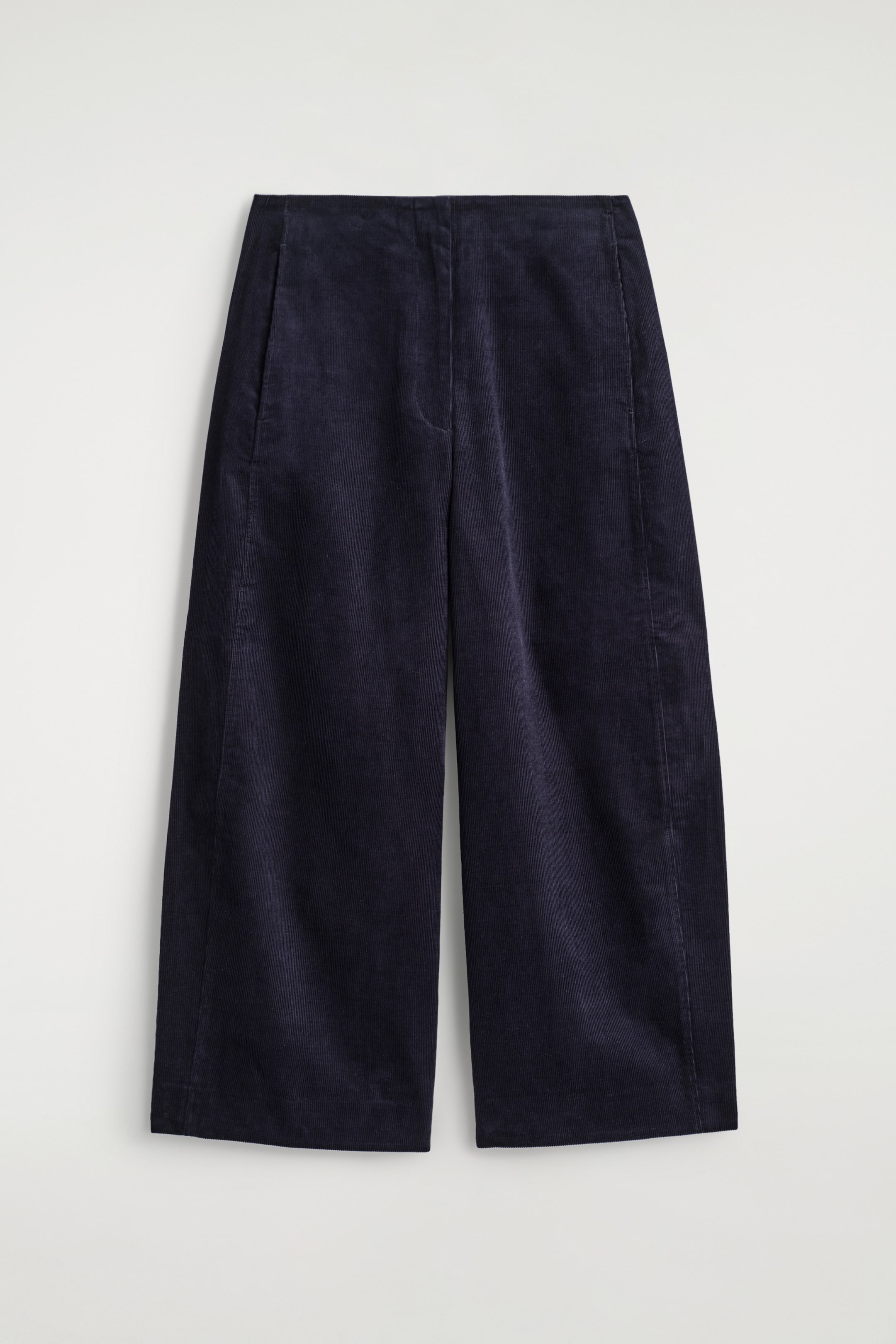 Ver imagen más grande: Un par de pantalones de pana azul oscuro se muestra de frente. Los pantalones presentan una pretina limpia, bolsillos laterales sutiles y una silueta de pierna ancha y recortada. El ribete vertical visible y las costuras superiores tonales detallan la tela y las costuras laterales.