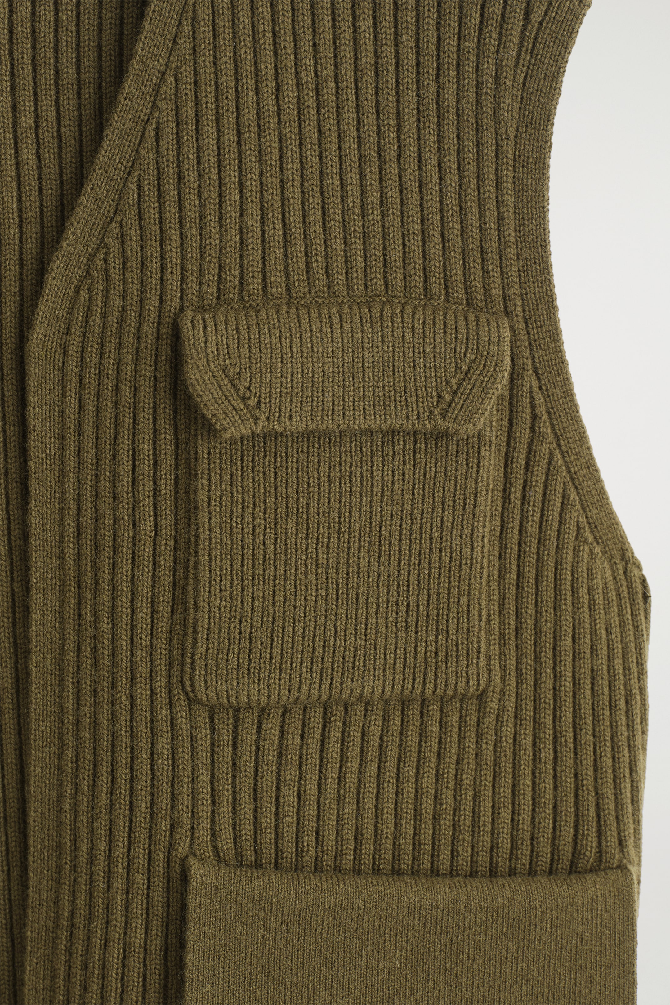 View larger image: An olive green, rib-knitted vest is being shown from the front, featuring a flap pocket with a V-shaped stitch on its flap, and a rectangular patch pocket positioned below it.