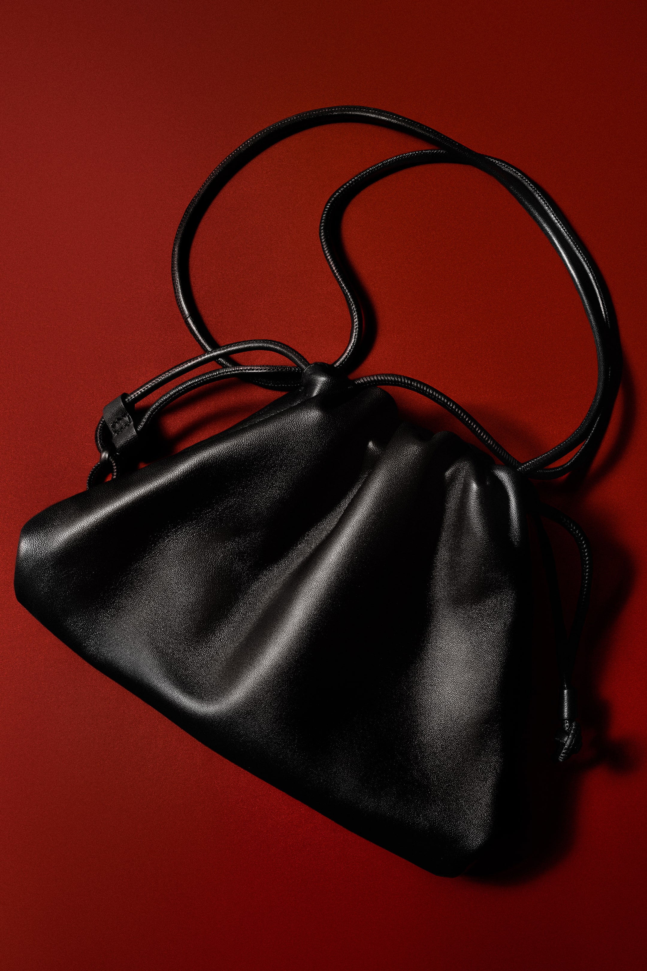 Преглед на по-голямо изображение: Мини чантата Cavatelli Clutch от черна кожа е представена отпред с меко набран, набран дизайн тип торбичка. Тя е с тънка, тръбовидна кожена презрамка за рамо и съответстващо закопчаване с шнур.