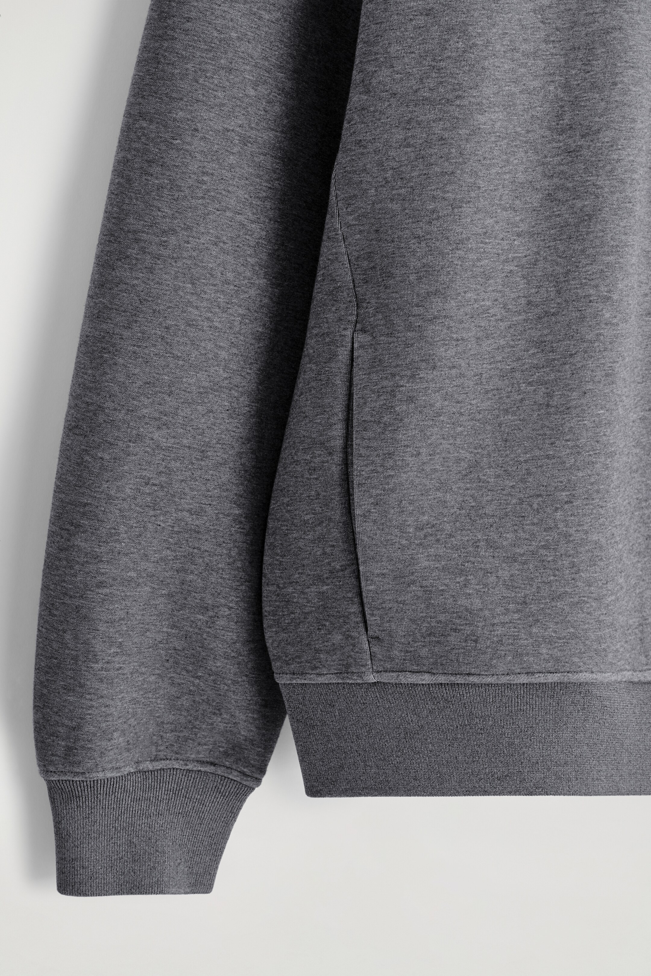 Zobrazit větší obrázek: Tmavě šedý pletený oděv má žebrované manžety a lem, s viditelným svislým otvorem kapsy na švu na boku.