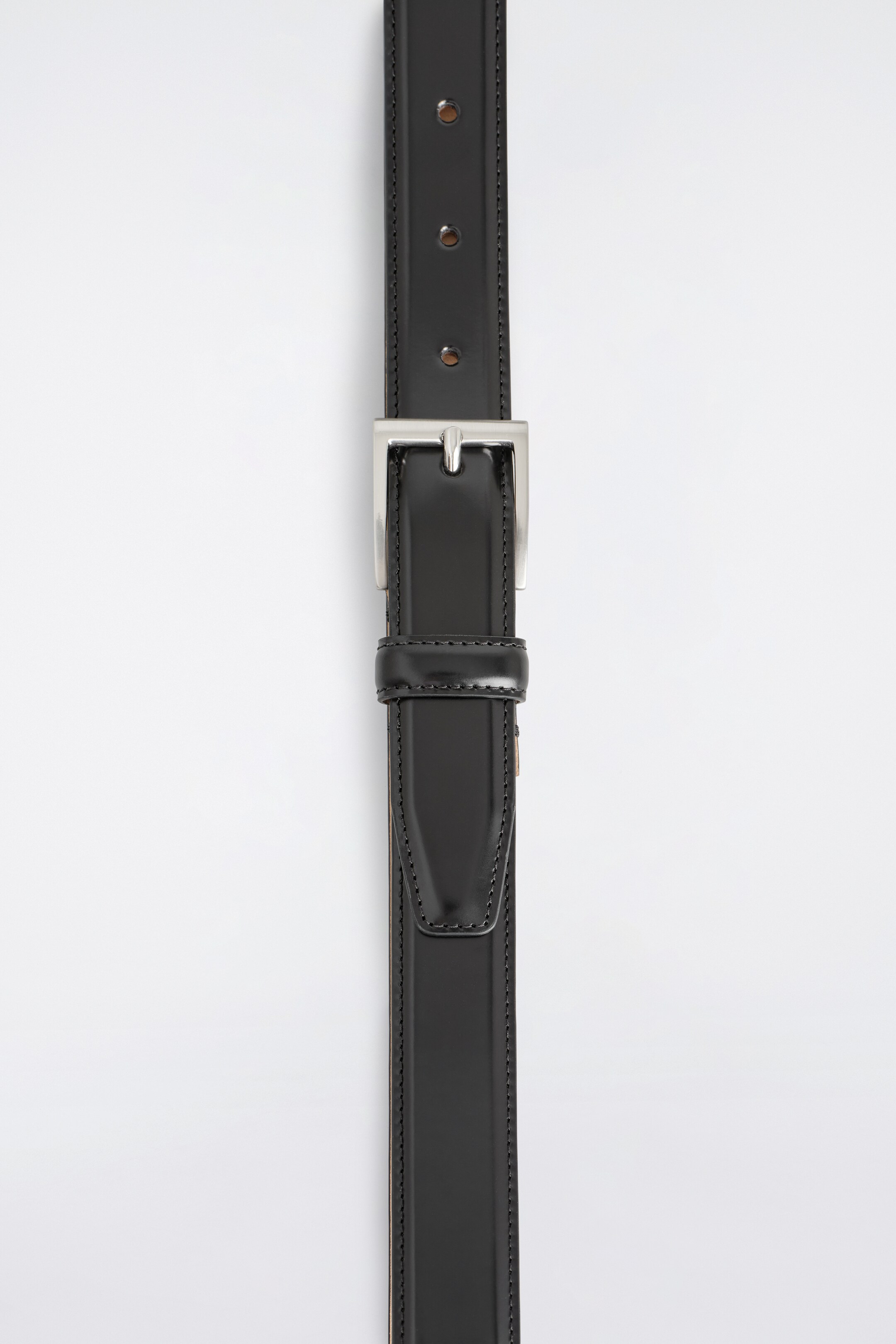 View larger image: A black leather belt is lying flat, viewed from the TOP, featuring a rectangular brushed silver-tone buckle, a single leather keeper, and visible edge stitching. Several adjustment holes are also visible on the strap.