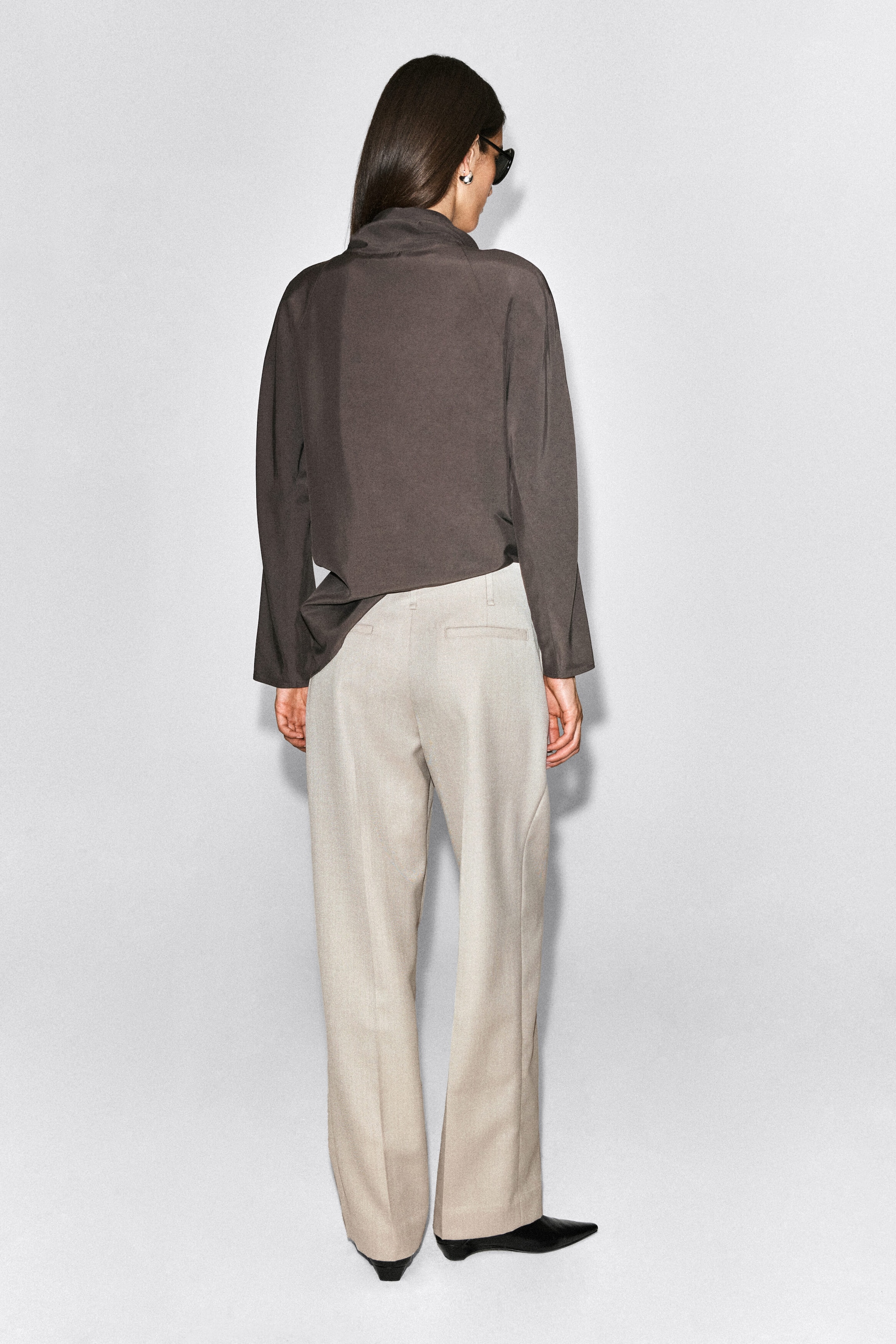 Light beige wool-blend trousers featuring a straight-leg cut and rear welt pockets are worn by the model, who is standing with their back to the camera. The trousers are styled with a dark gray long-sleeve top and pool slightly over black pointed-toe shoes. Light beige wool-blend trousers featuring a straight-leg cut and rear welt pockets are worn by the model, who is standing with their back to the camera. The trousers are styled with a dark gray long-sleeve top and pool slightly over black pointed-toe shoes.