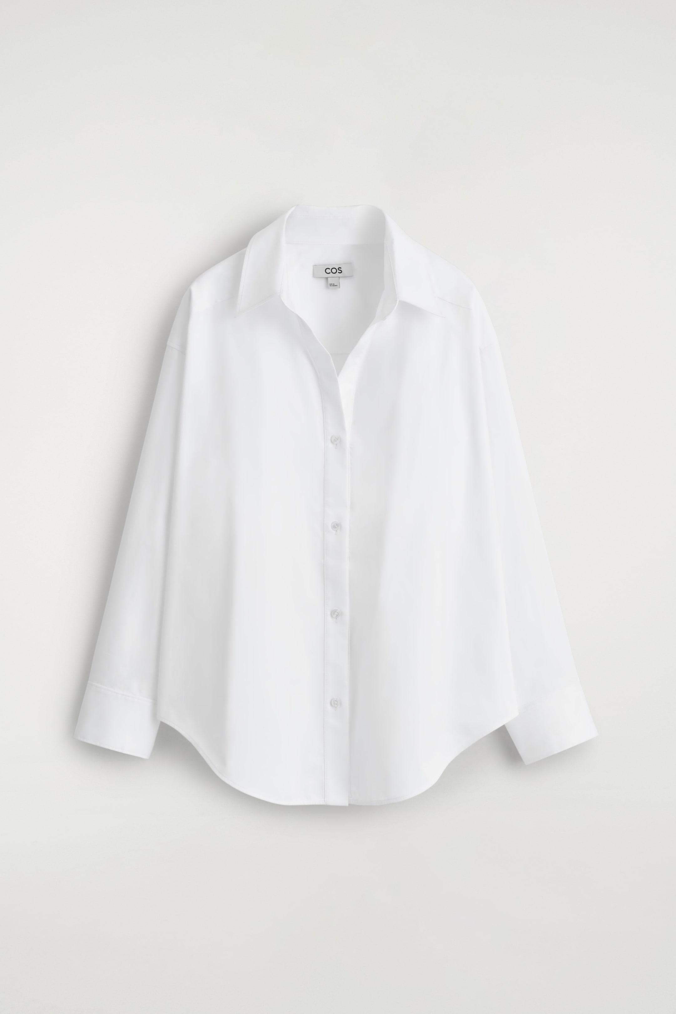 Grotere afbeelding bekijken: Een wit shirt met een relaxte pasvorm toont zijn voorkant, met een open puntkraag en een zichtbare knopenlijst met witte knopen aan de voorkant. Het heeft lange mouwen en een afgeronde zoom.