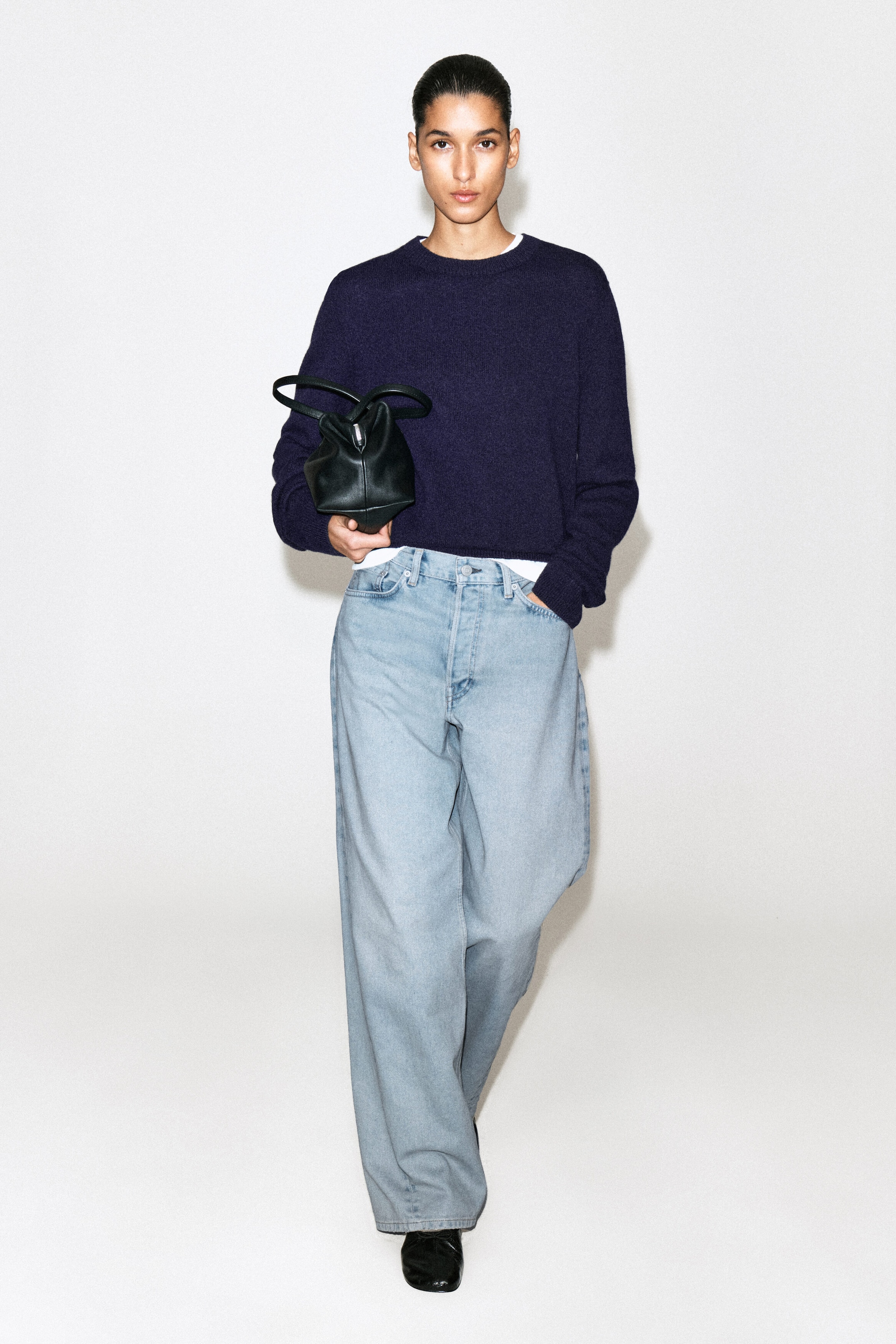 The Facade straight-leg jeans are shown in a relaxed, wide-leg silhouette in a light blue denim wash from the front. The high-waisted jeans fit loosely through the leg and pool slightly over black shoes, styled with a dark purple jumper resting at the waistband.