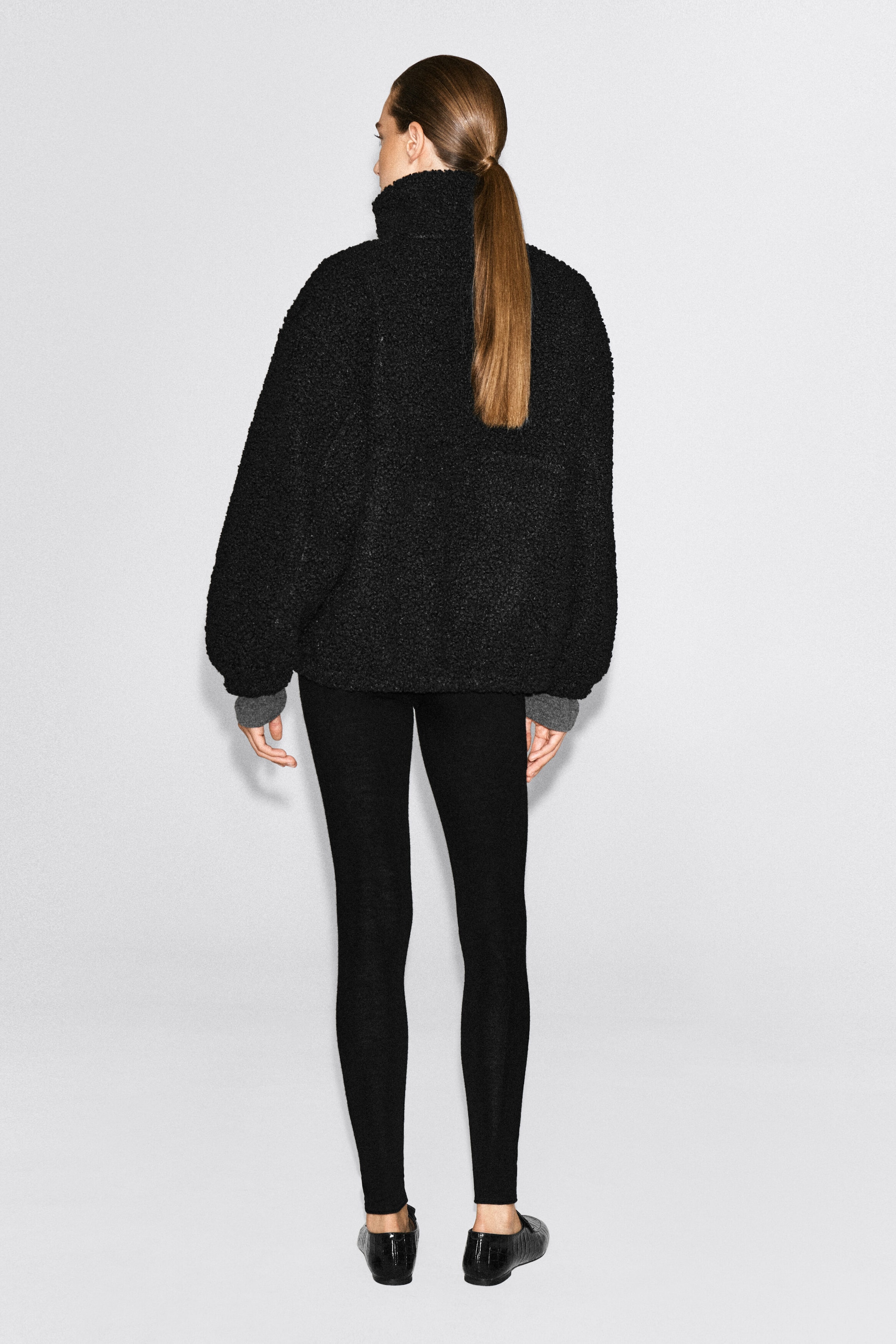 Un chandail teddy noir à col cheminée est porté par le mannequin, montré de dos afin de mettre en valeur son tissu en molleton texturé et sa silhouette décontractée. Le chandail présente un col montant et est porté avec des leggings noirs, tandis que des poignets côtelés gris dépassent des manches. Un chandail teddy noir à col cheminée est porté par le mannequin, montré de dos afin de mettre en valeur son tissu en molleton texturé et sa silhouette décontractée. Le chandail présente un col montant et est porté avec des leggings noirs, tandis que des poignets côtelés gris dépassent des manches.