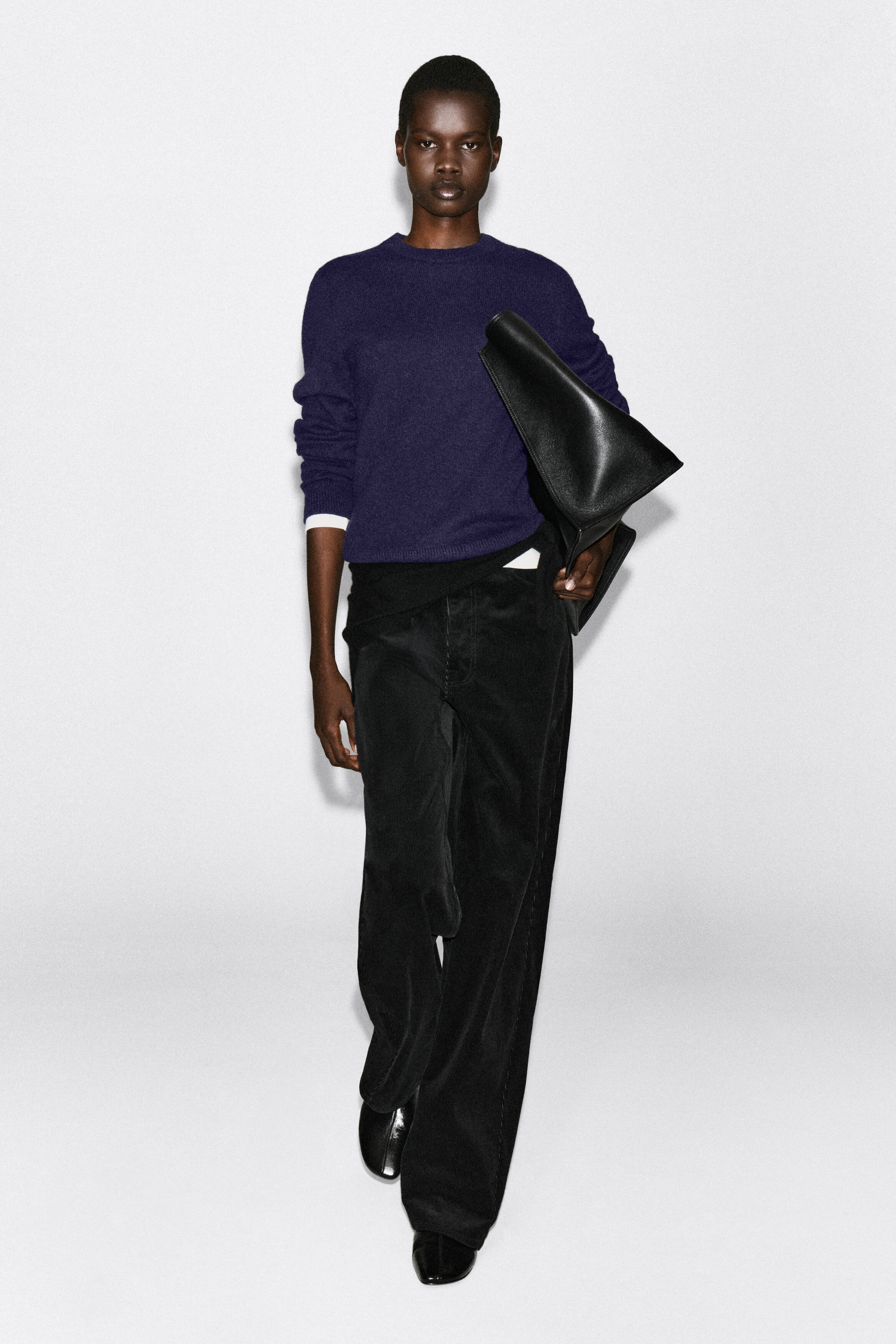 Un pull en cachemire à col rond d’un violet foncé est porté par le mannequin, avec une coupe classique et des finitions côtelées au niveau du col et des poignets. Le pull est associé à une couche blanche visible aux manches et à l’ourlet, ainsi qu’à un pantalon noir à jambes larges et à un sac en cuir noir porté sous le bras. Un pull en cachemire à col rond d’un violet foncé est porté par le mannequin, avec une coupe classique et des finitions côtelées au niveau du col et des poignets. Le pull est associé à une couche blanche visible aux manches et à l’ourlet, ainsi qu’à un pantalon noir à jambes larges et à un sac en cuir noir porté sous le bras.