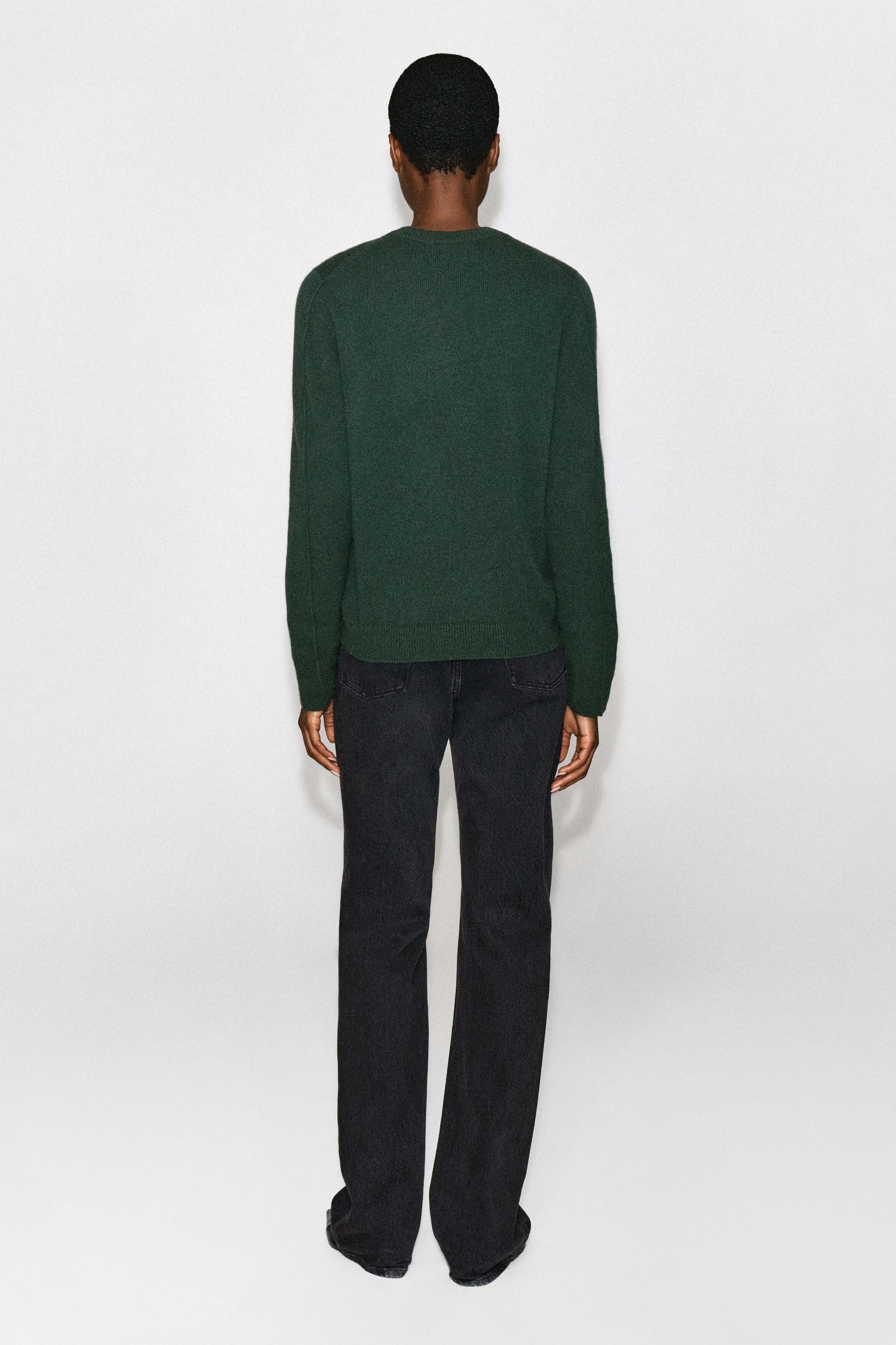The model is wearing a dark green cashmere crewneck sweater, shown from the back, paired with dark gray straight-leg jeans. The long-sleeve sweater features a relaxed fit with ribbed hem and cuffs. The model is wearing a dark green cashmere crewneck sweater, shown from the back, paired with dark gray straight-leg jeans. The long-sleeve sweater features a relaxed fit with ribbed hem and cuffs.