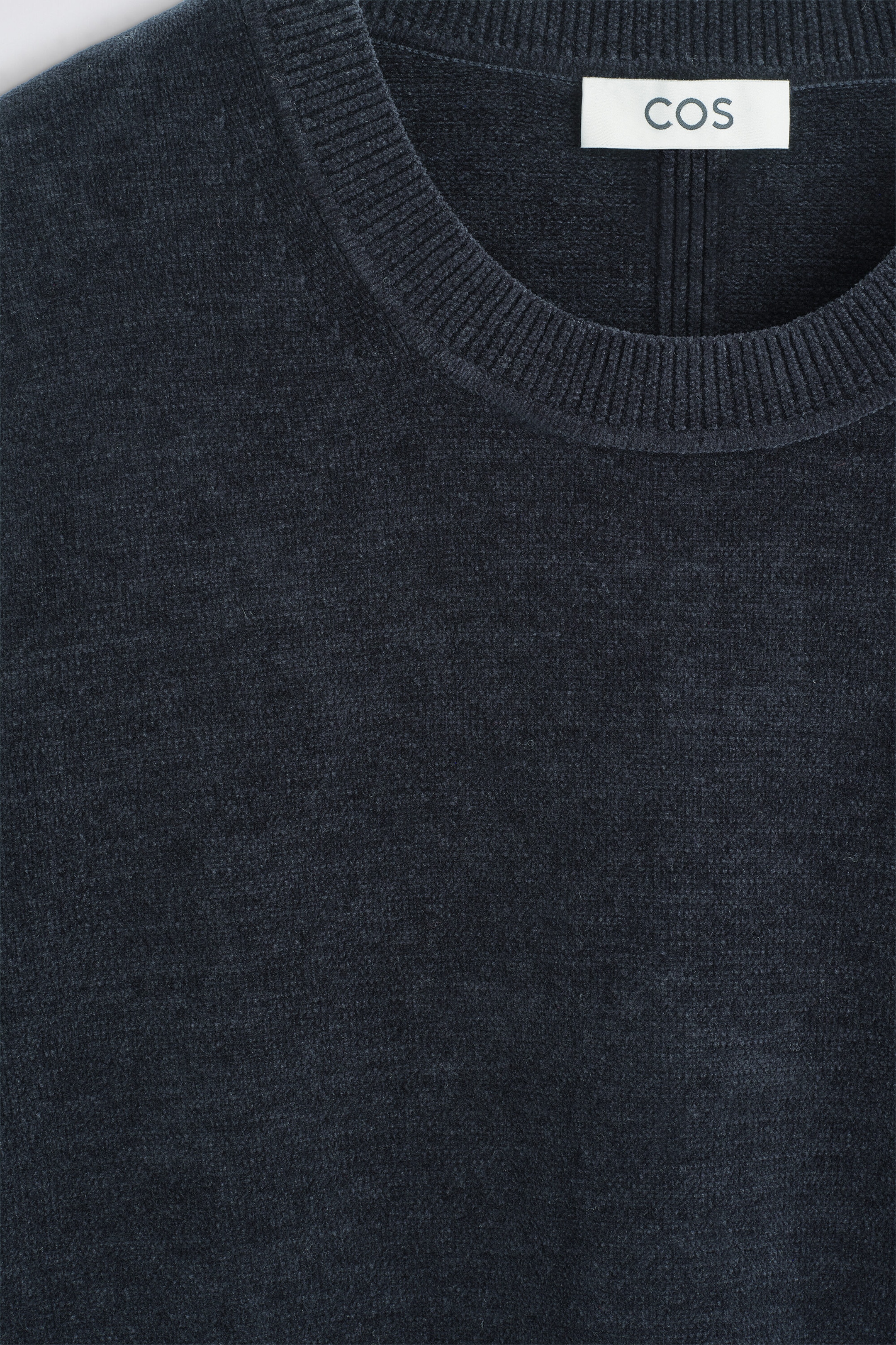 The cotton-chenille crew-neck jumper features a soft, velvety texture in a dark navy-grey shade. This close-up front view highlights the ribbed crew-neck collar and a white COS brand label stitched on the inner neckline. The cotton-chenille crew-neck jumper features a soft, velvety texture in a dark navy-grey shade. This close-up front view highlights the ribbed crew-neck collar and a white COS brand label stitched on the inner neckline.