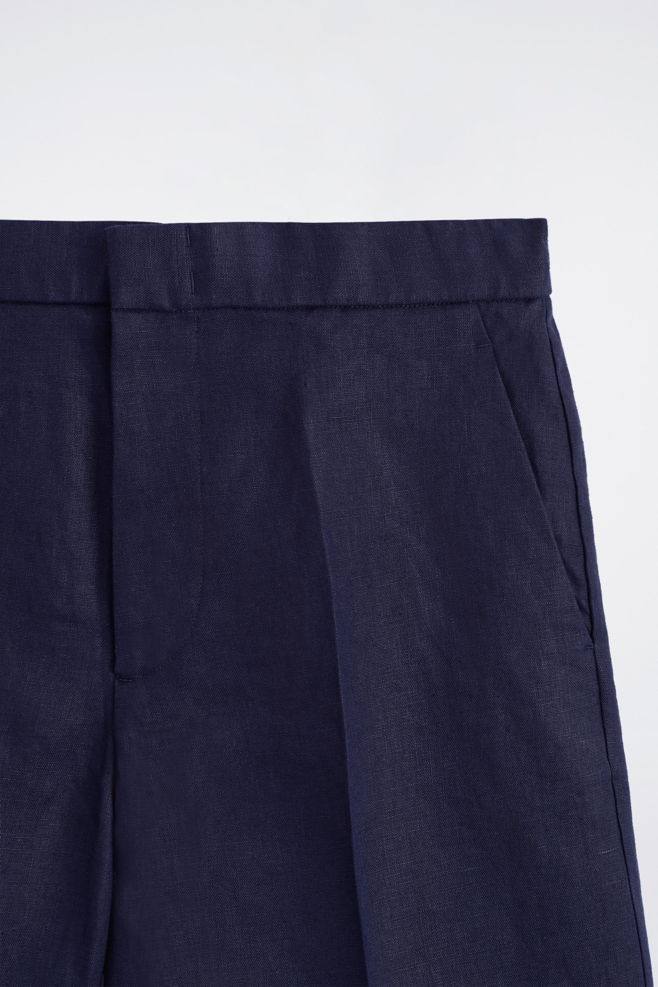Visualizza immagine più grande: I pantaloncini in lino blu navy sono mostrati frontalmente, caratterizzati da una cintura piatta, una chiusura con gancio, barra e zip, e tasche laterali a cucitura. Il tessuto presenta una texture di lino visibile.