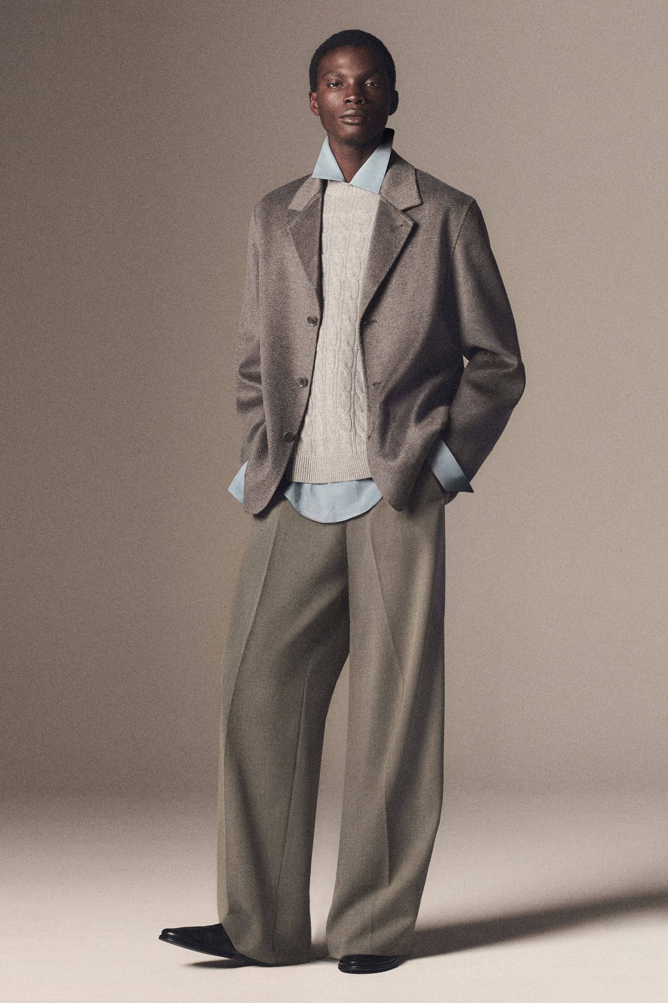 The Tailored Double-Faced Pure Cashmere Blazer and Wool-Blend Relaxed-Fit Wide-Leg Trousers are featured in a front-facing view on a model. The taupe blazer showcases a relaxed, softly structured drape with notch lapels, layered over a beige cable-knit jumper and a light-blue collared shirt. The olive-grey trousers present a relaxed-fit, wide-leg silhouette with sharp front creases that fall slightly over black shoes. The Tailored Double-Faced Pure Cashmere Blazer and Wool-Blend Relaxed-Fit Wide-Leg Trousers are featured in a front-facing view on a model. The taupe blazer showcases a relaxed, softly structured drape with notch lapels, layered over a beige cable-knit jumper and a light-blue collared shirt. The olive-grey trousers present a relaxed-fit, wide-leg silhouette with sharp front creases that fall slightly over black shoes.
