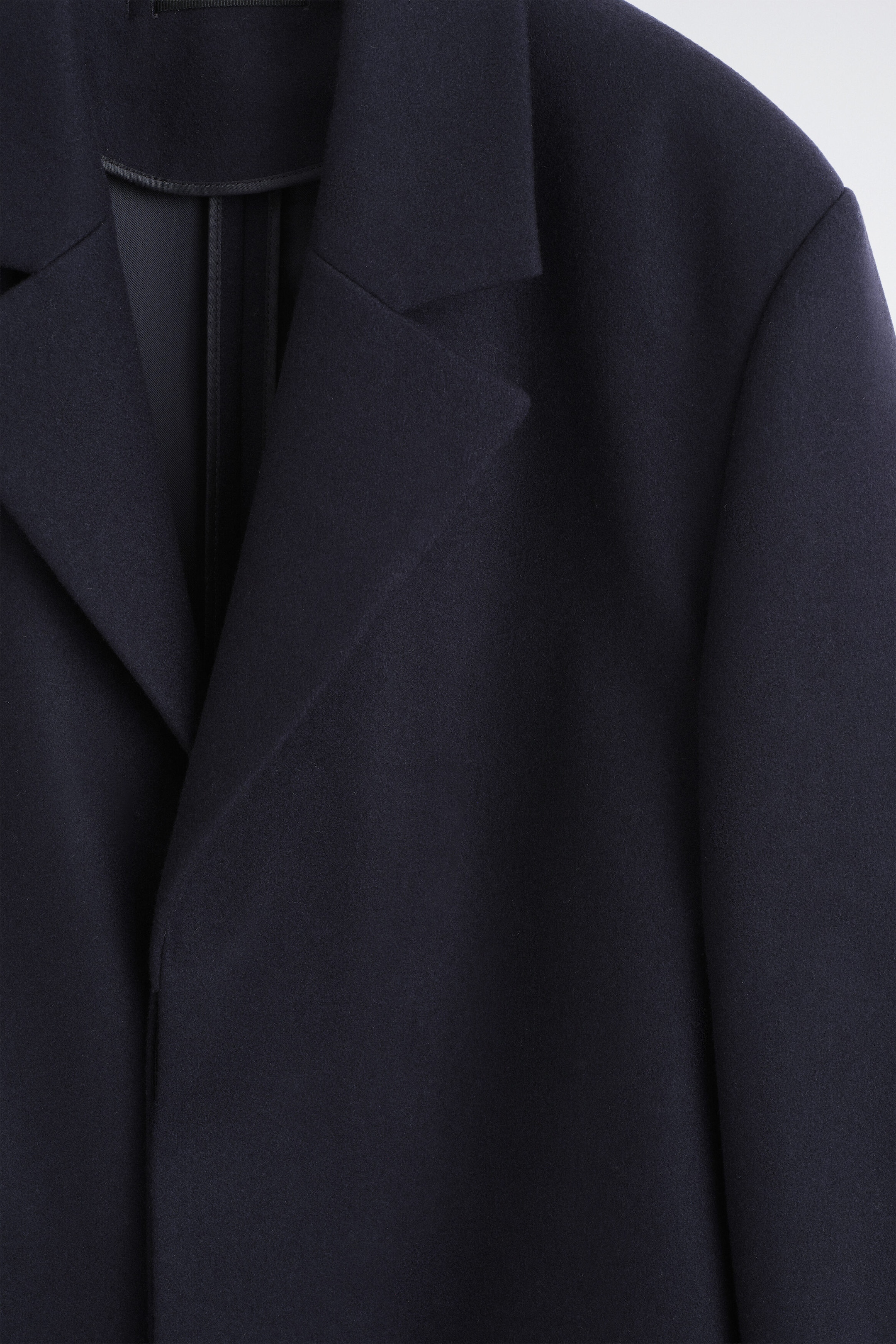 A dark blue coat features wide notch lapels and structured shoulders, presenting its front upper section. The fabric displays a smooth, dense texture. A dark blue coat features wide notch lapels and structured shoulders, presenting its front upper section. The fabric displays a smooth, dense texture.