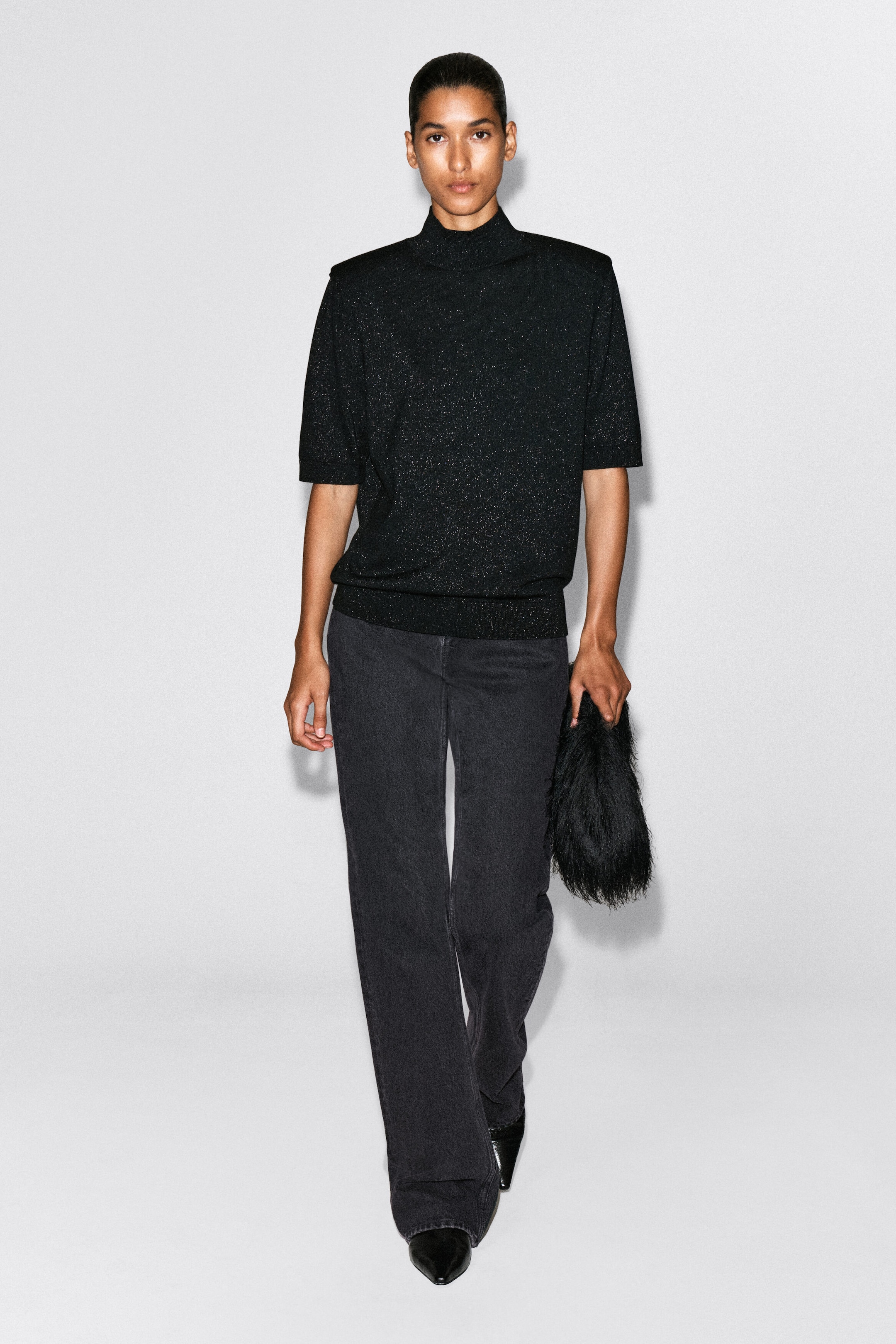 The black knitted mock-neck T-shirt with subtle metallic flecks is showcased in a regular fit from the front, featuring sculpted shoulders and elbow-length sleeves. The top features a ribbed mock neck and a ribbed hem, styled with dark grey jeans. The black knitted mock-neck T-shirt with subtle metallic flecks is showcased in a regular fit from the front, featuring sculpted shoulders and elbow-length sleeves. The top features a ribbed mock neck and a ribbed hem, styled with dark grey jeans.