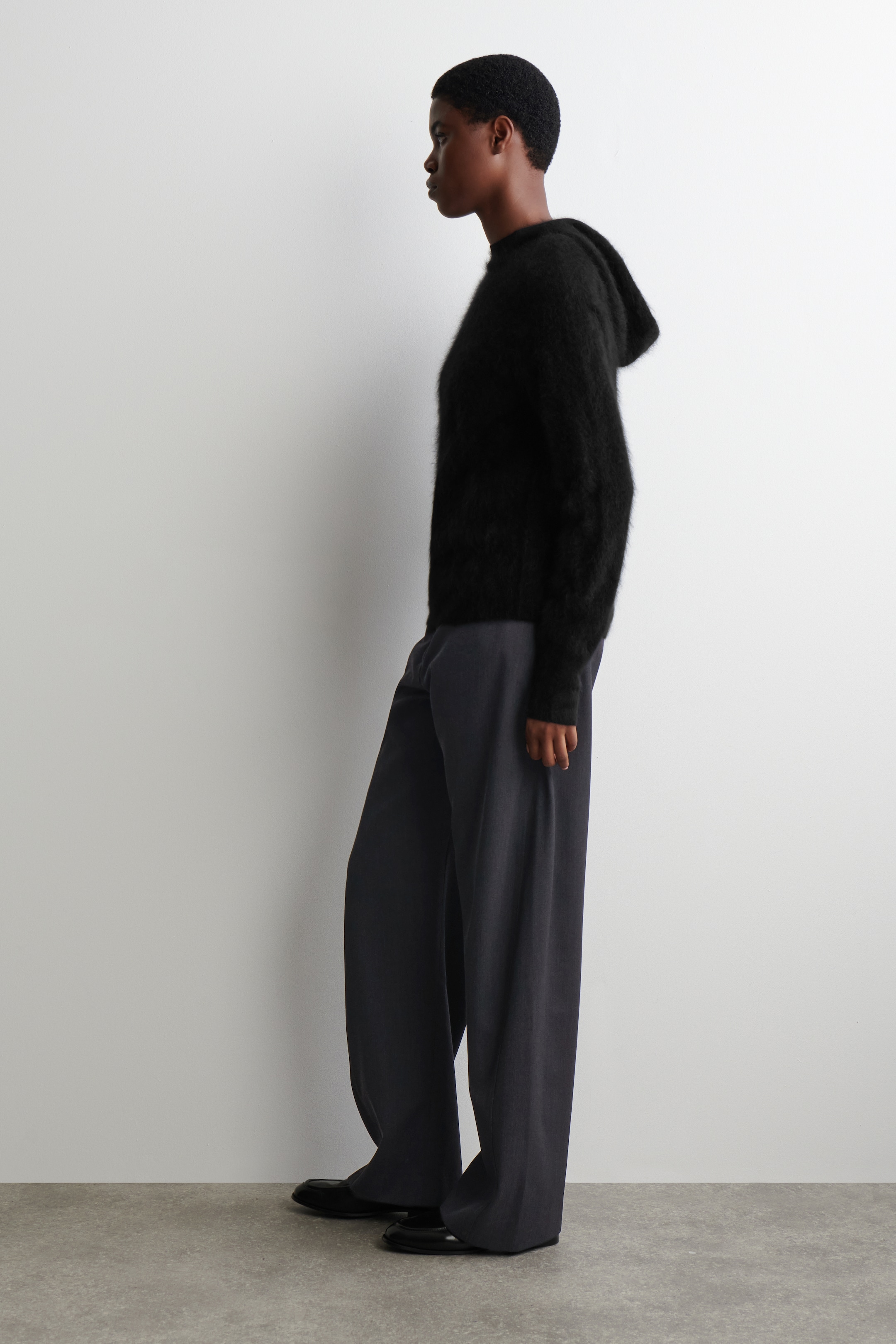 View larger image: A black fuzzy hooded sweater is being worn with dark grey wide-leg trousers and black flat shoes, all seen from a side profile.