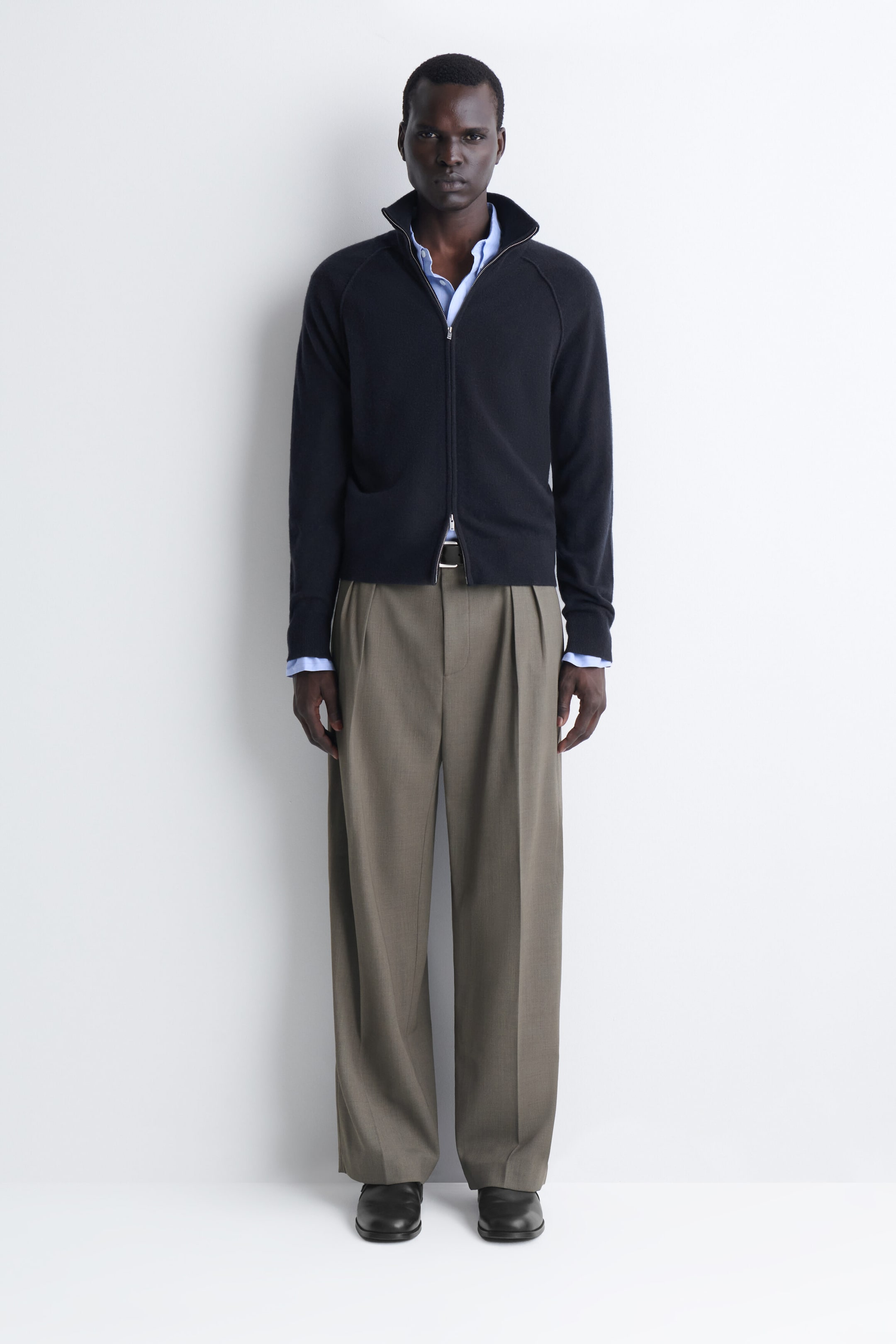 The navy cashmere funnel-neck zip-up cardigan is shown in a front-facing fit, featuring a two-way zip fastening and raglan sleeves with ribbed cuffs. It is worn layered over a light blue collared shirt, with the collar and cuffs peeking out. The navy cashmere funnel-neck zip-up cardigan is shown in a front-facing fit, featuring a two-way zip fastening and raglan sleeves with ribbed cuffs. It is worn layered over a light blue collared shirt, with the collar and cuffs peeking out.