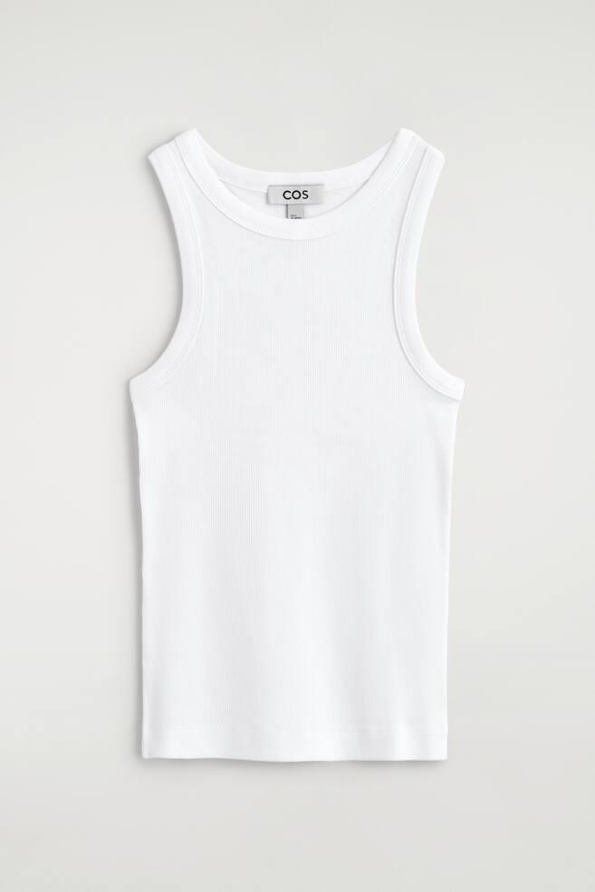 Ein weißes Tanktop wird flach liegend von vorne gezeigt. Es verfügt über einen runden Halsausschnitt, breite Schulterträger und eine fein gerippte Textur, mit einem "COS"-Markenetikett, das am hinteren Halsbereich sichtbar ist. - 1