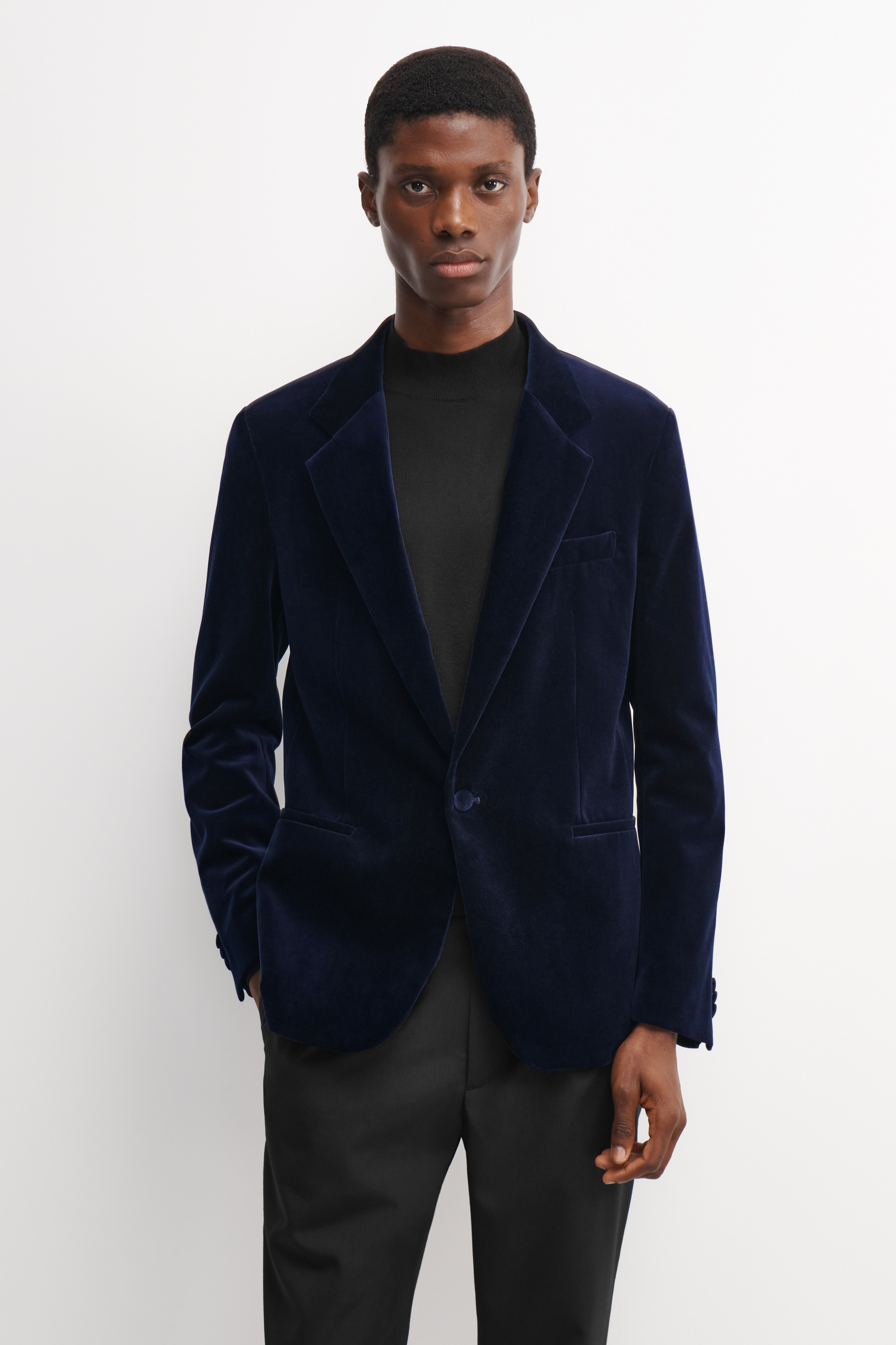 Un blazer da smoking in velluto blu navy Ã¨ mostrato frontalmente, con design monopetto, revers a lancia, chiusura a un bottone e tasche a filetto frontali.
