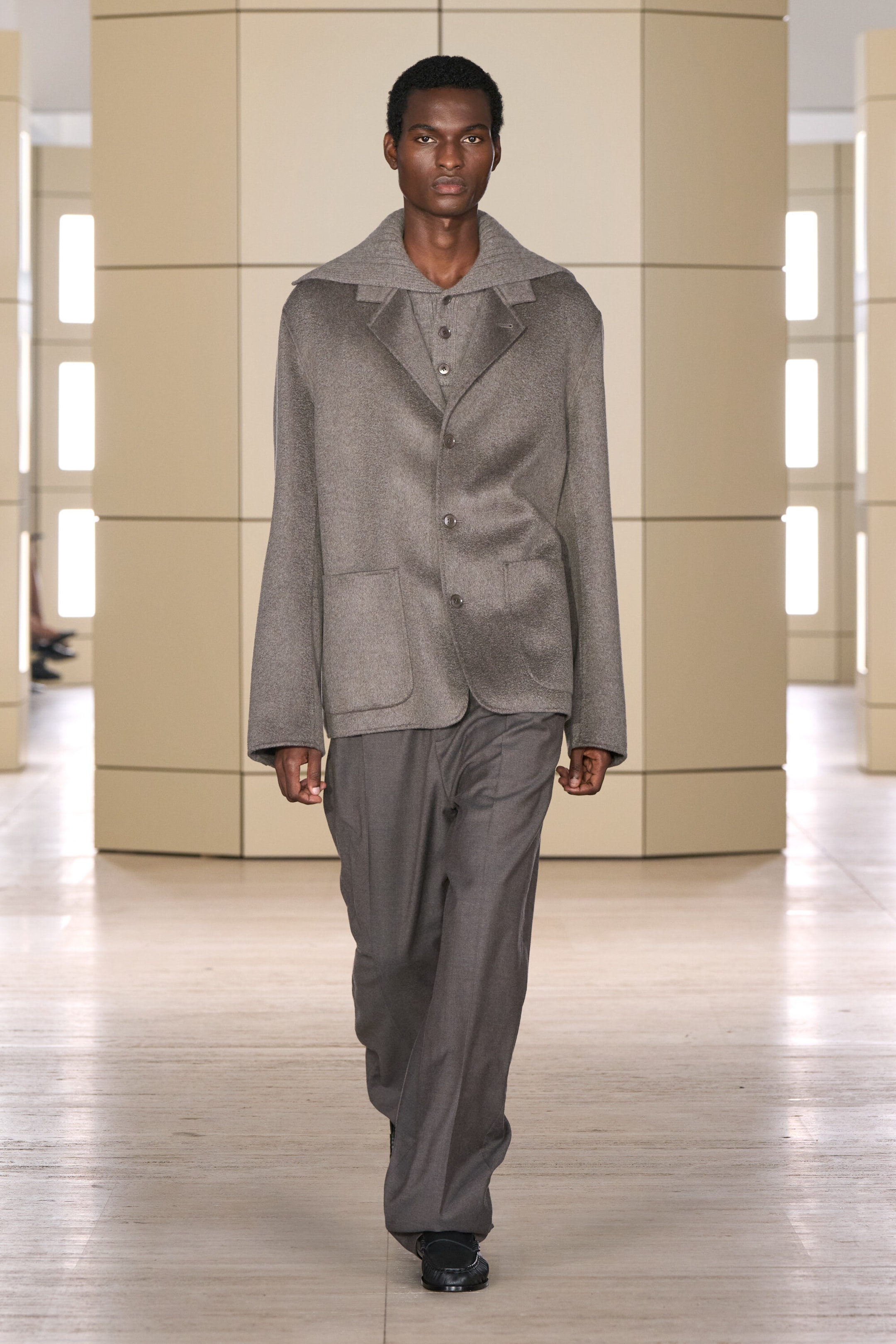 The front-facing tailored double-faced cashmere blazer in medium grey features notch lapels, a four-button closure, and front patch pockets, layered over a grey knit collar. It is paired with dark grey wool-flannel relaxed-fit straight-leg pants that drape loosely.