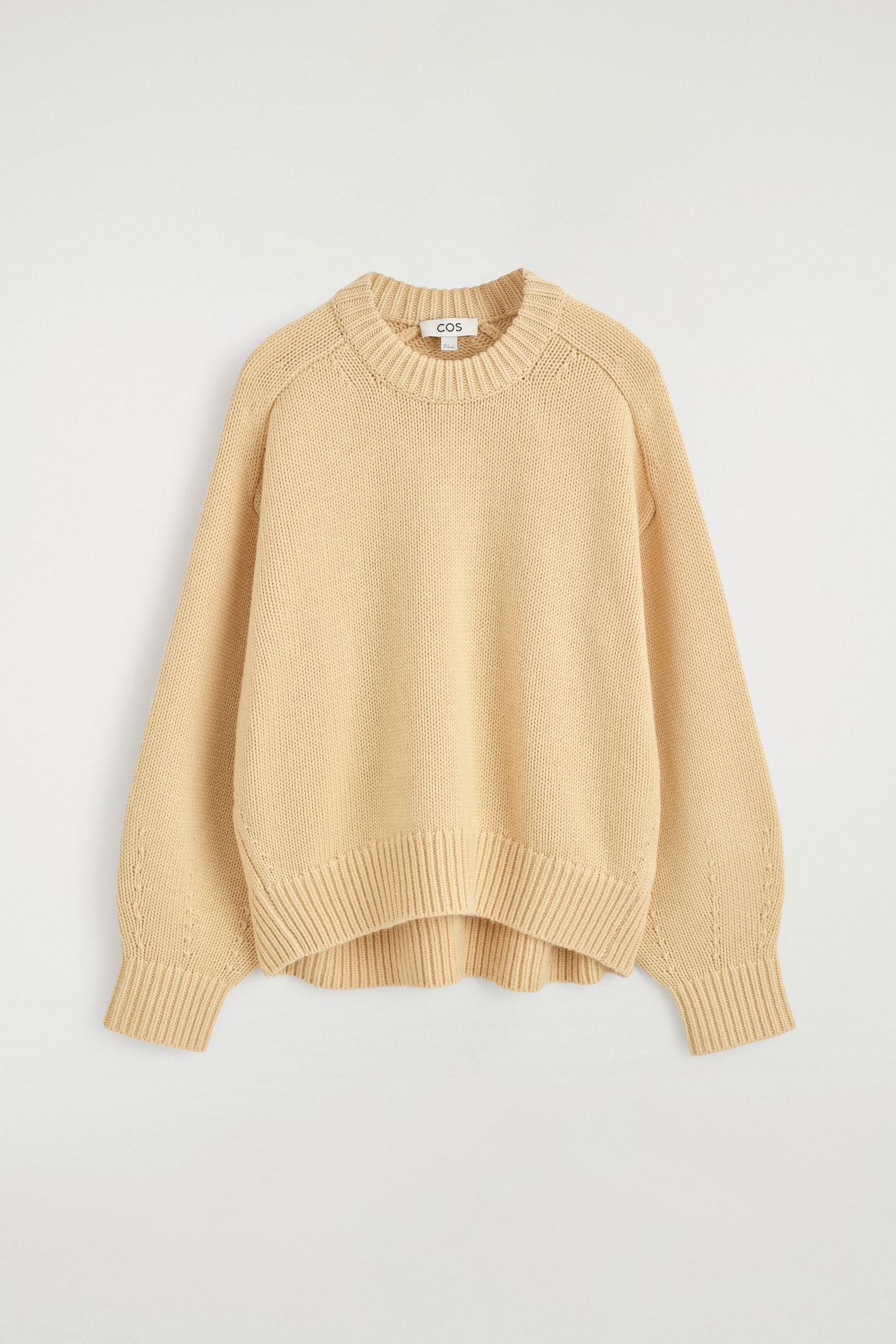 Le chandail à col rond en laine est présenté de face, avec un tricot pâle jaune de poids moyen, une encolure ronde côtelée épaisse et des manches raglan arrondies. Le modèle affiche de longs poignets côtelés larges et un ourlet côtelé assorti.