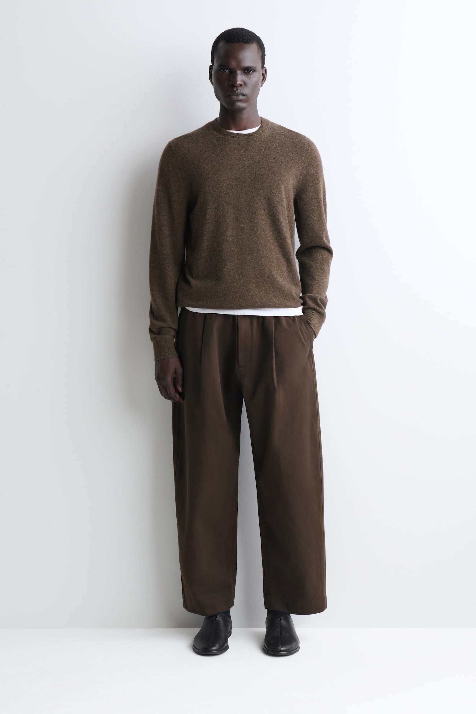 Diese plissierte Barrel-Leg-Hose in entspannter Passform in Dunkelbraun ist von vorne zu sehen und verfÃ¼gt Ã¼ber einen elastischen Bund mit zentralem Knopfverschluss. Das Design zeigt eine legere, zum Saum hin schmal zulaufende Silhouette mit vorderen Falten, die fÃ¼r strukturiertes Volumen sorgen. - 1