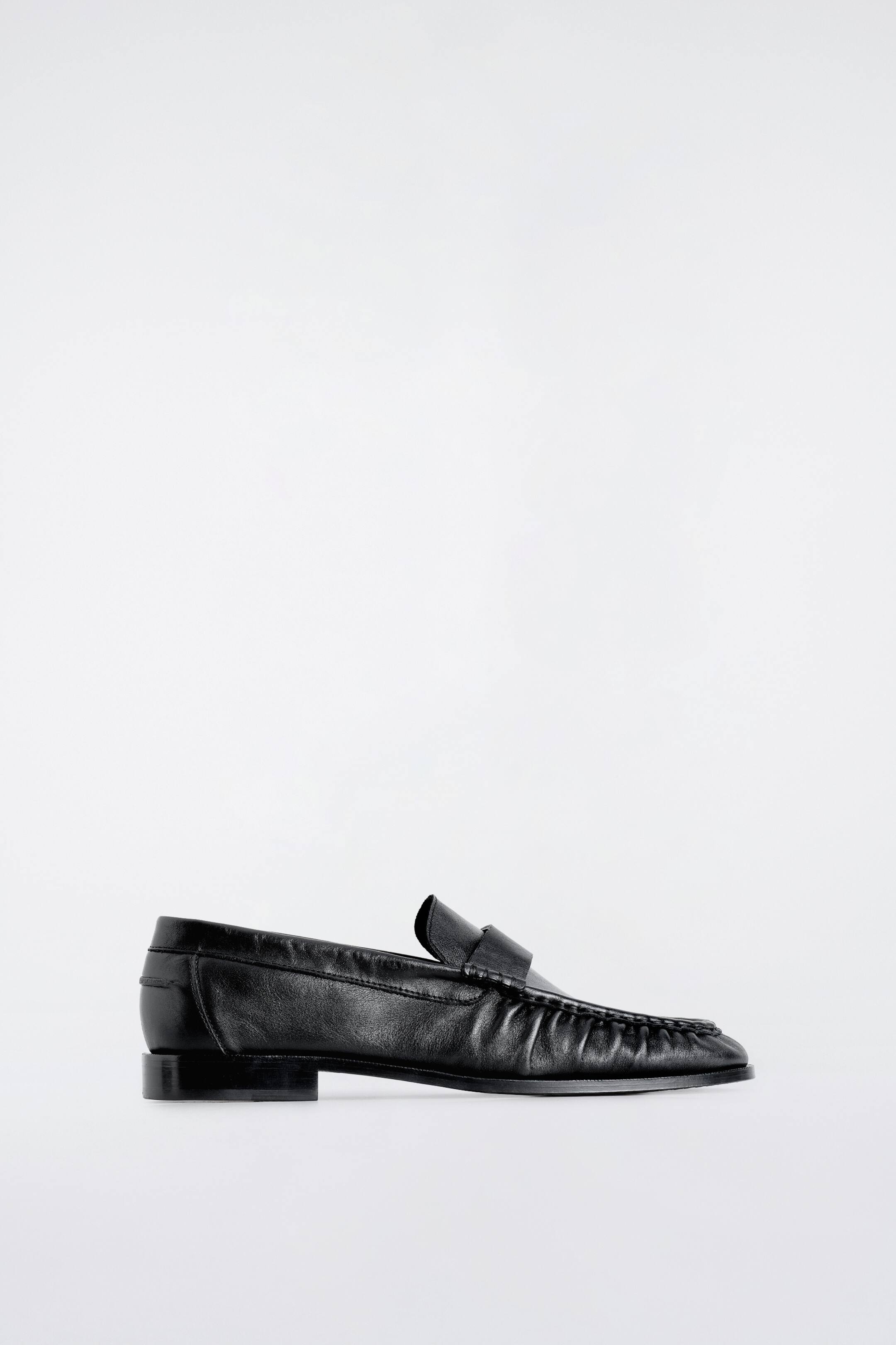 Ver imagem maior: Um loafer em pele preta é apresentado de perfil lateral, exibindo um perfil suavemente franzido sobre a gáspea. Inclui uma tira tipo penny loafer e um salto baixo e recuado.