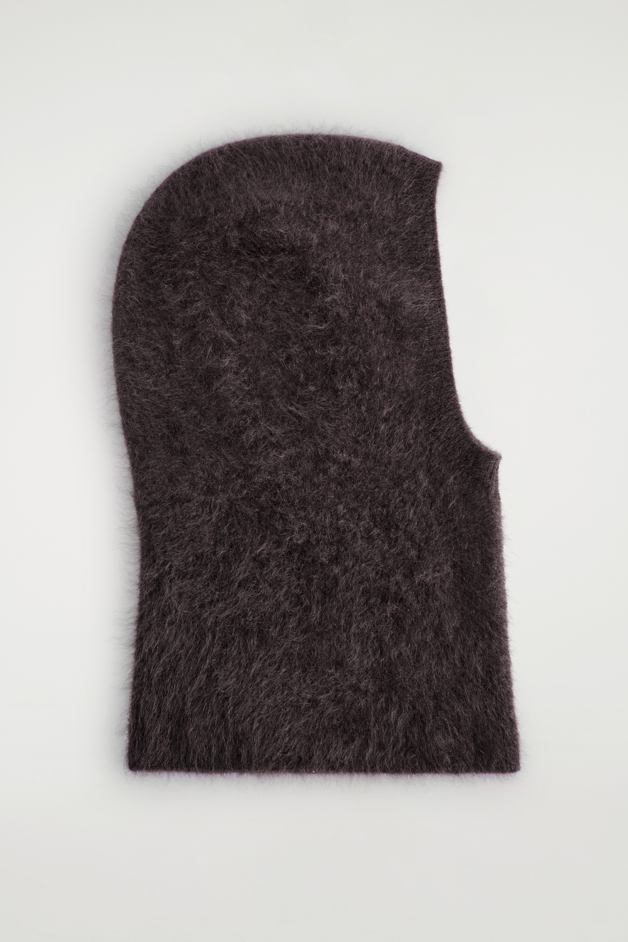 Agrandir l'image: Une cagoule brun foncé est posée à plat, sa surface présente une texture douce, duveteuse et tricotée brossée. Elle présente un sommet arrondi et une grande ouverture unique pour le visage.