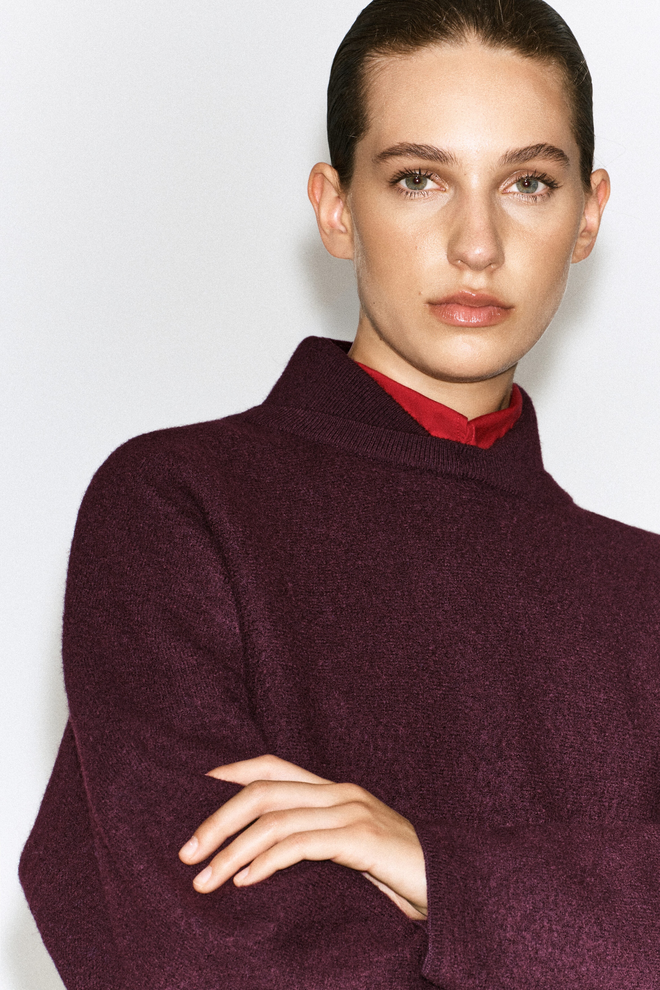 Un chandail en laine bouillie à col superposé, de couleur bordeaux foncé, est porté par le mannequin, les bras croisés. Le chandail présente un col montant structuré superposé à un col rouge vif visible en dessous. Un chandail en laine bouillie à col superposé, de couleur bordeaux foncé, est porté par le mannequin, les bras croisés. Le chandail présente un col montant structuré superposé à un col rouge vif visible en dessous.