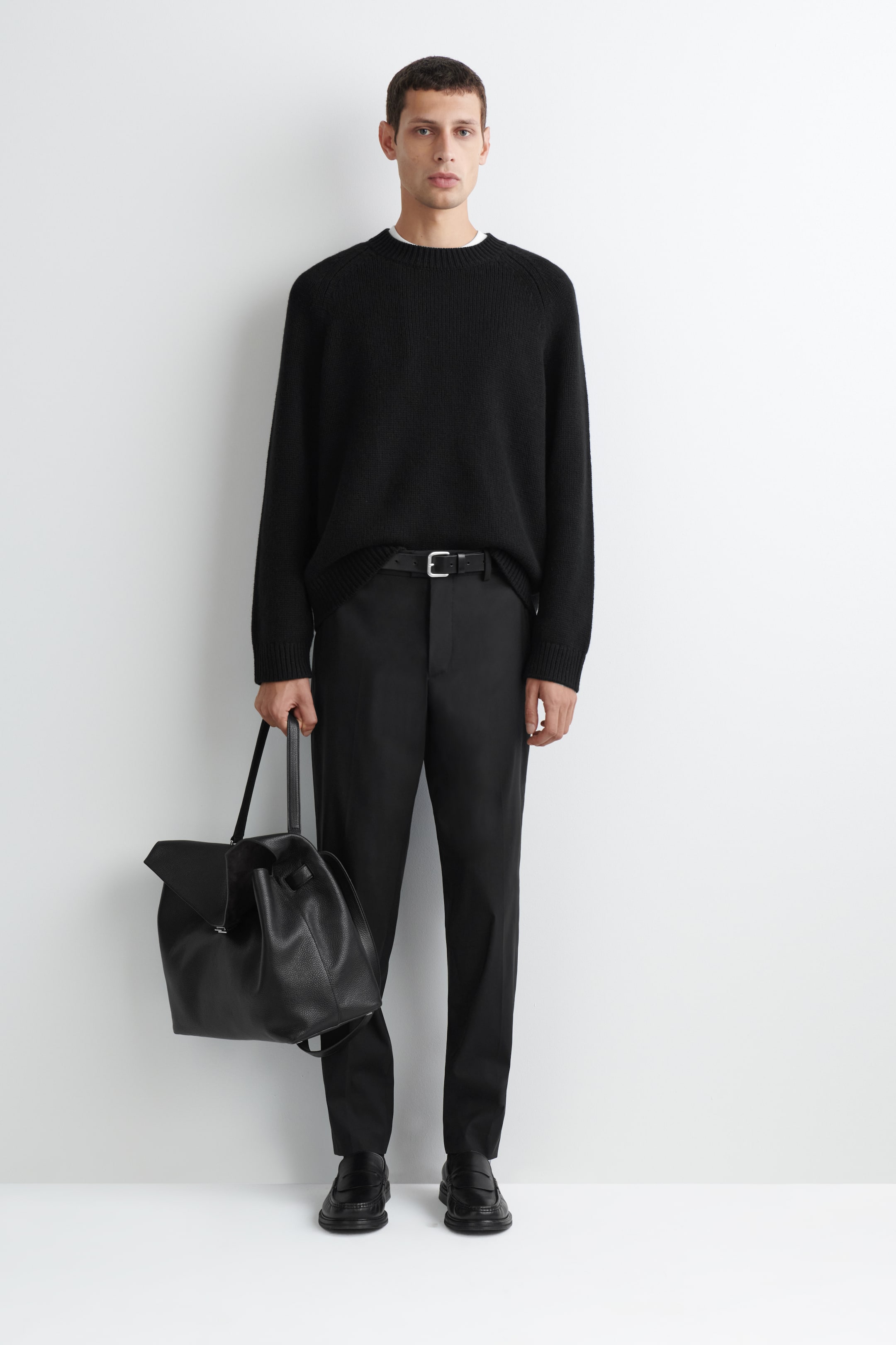 Vezi imaginea mai mare: Acești pantaloni drepți, slim-fit, din amestec de lână, sunt prezentați din față, evidențiind un design croit, cu dungi bine călcate pe fiecare picior. O curea neagră din piele, cu cataramă în nuanță argintie, este purtată prin găicile pentru curea, iar un pulover negru din tricot este băgat parțial în talie.