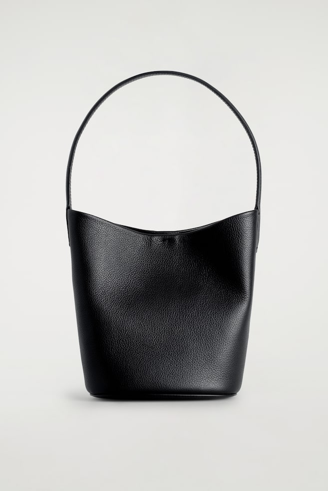 Un sac seau noir présente une texture grainée sur son corps, avec une unique fine poignée supérieure et une ouverture supérieure incurvée vers le bas au centre. - 1