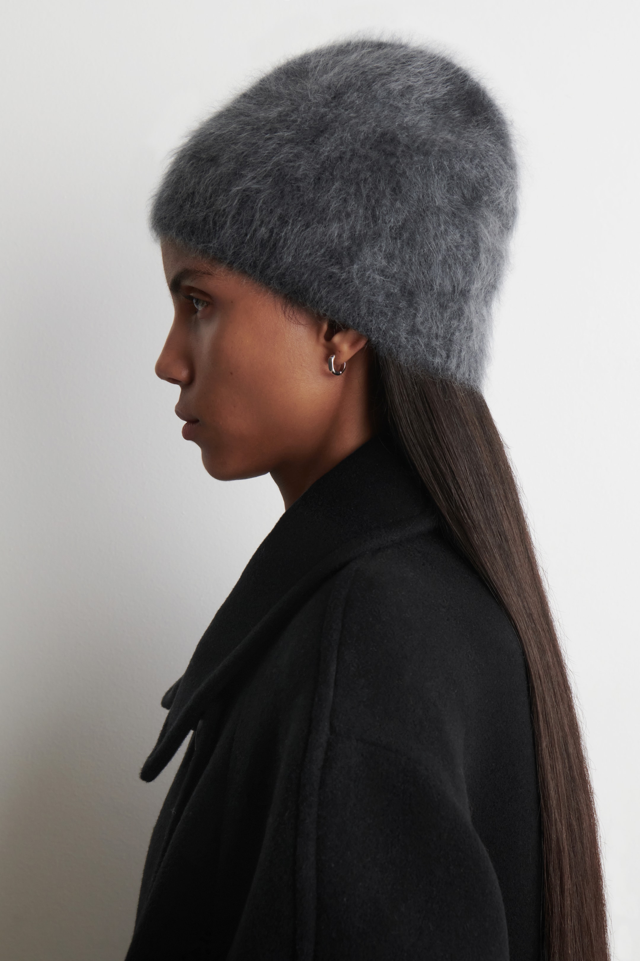 Agrandir l'image: Un bonnet en cachemire brossé de couleur charbon est porté sur une tête, vue depuis la GAUCHE. Sa texture duveteuse est visible alors qu'il couvre le haut et les côtés de la tête, et il repose contre le col d'un manteau noir.