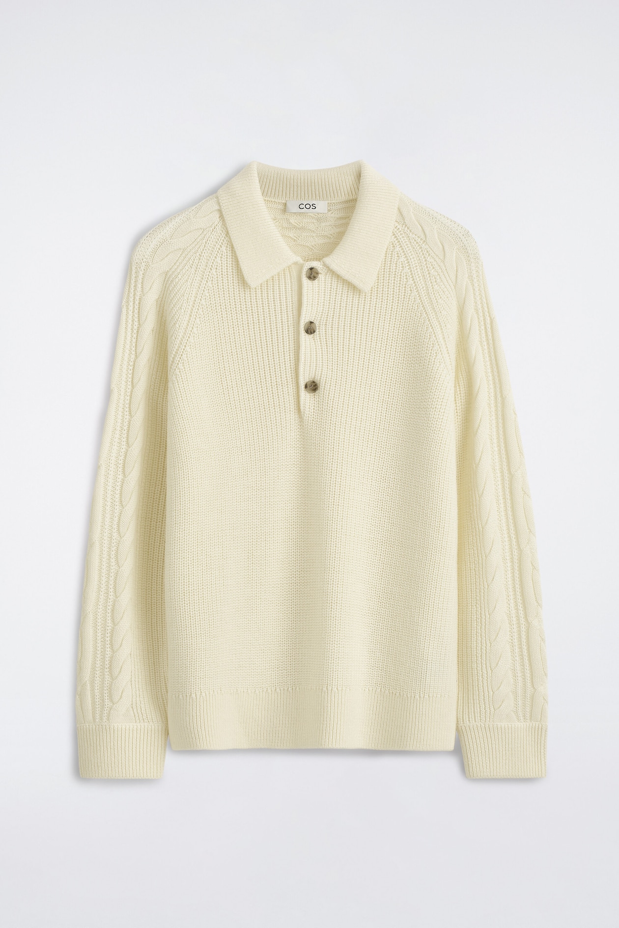 An off-white chunky knit polo sweater is shown from the front, featuring a classic collar, a three-button placket, and cable-knit details along the raglan shoulders and sleeves. The design is finished with a ribbed texture throughout the body, cuffs, and hem.