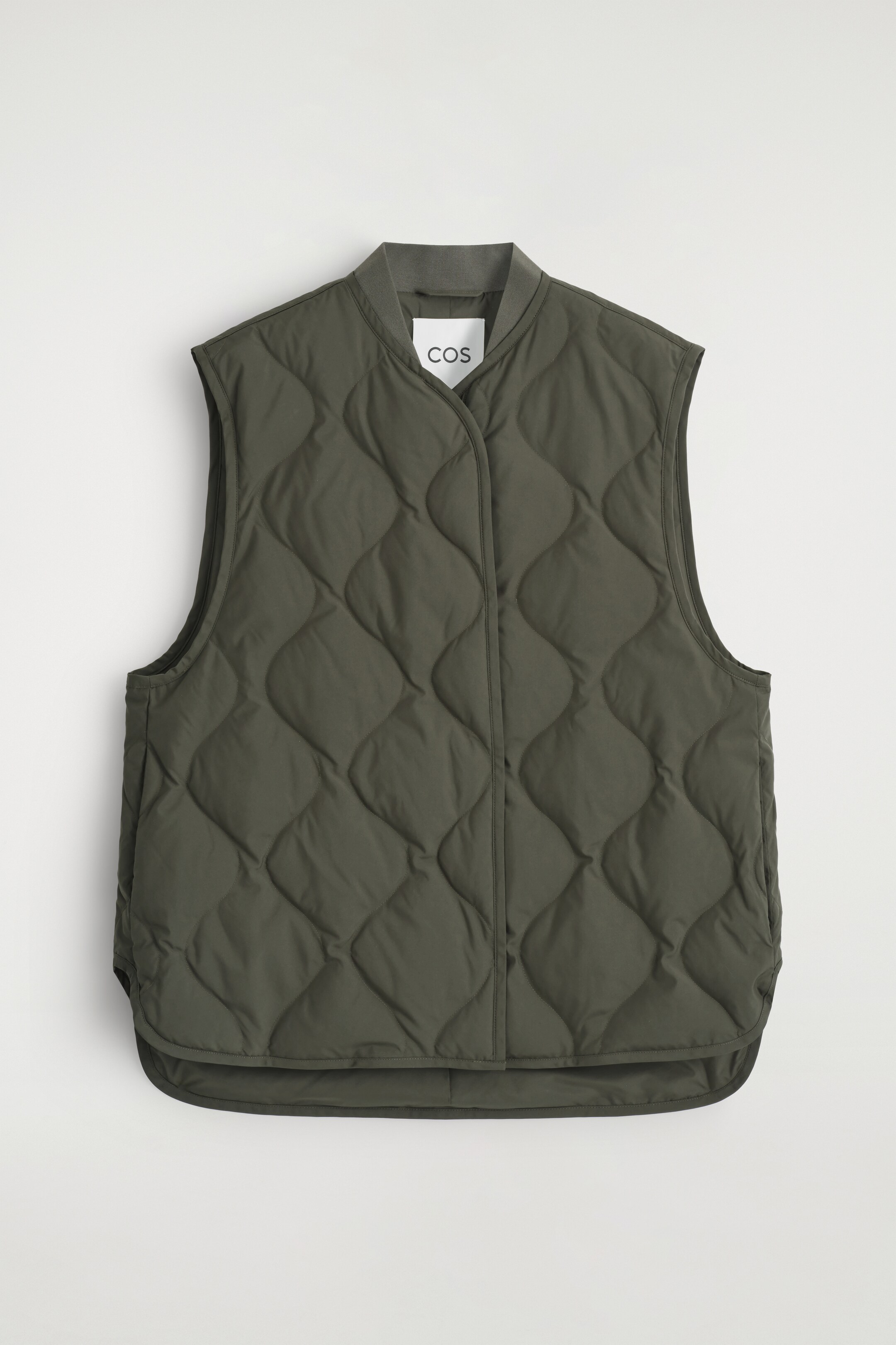 Agrandir l'image: Un gilet matelassé vert olive foncé est présenté à plat, face avant. Il présente un col bomber côtelé, une patte centrale dissimulant la fermeture, des poches latérales discrètes et un ourlet arrondi.