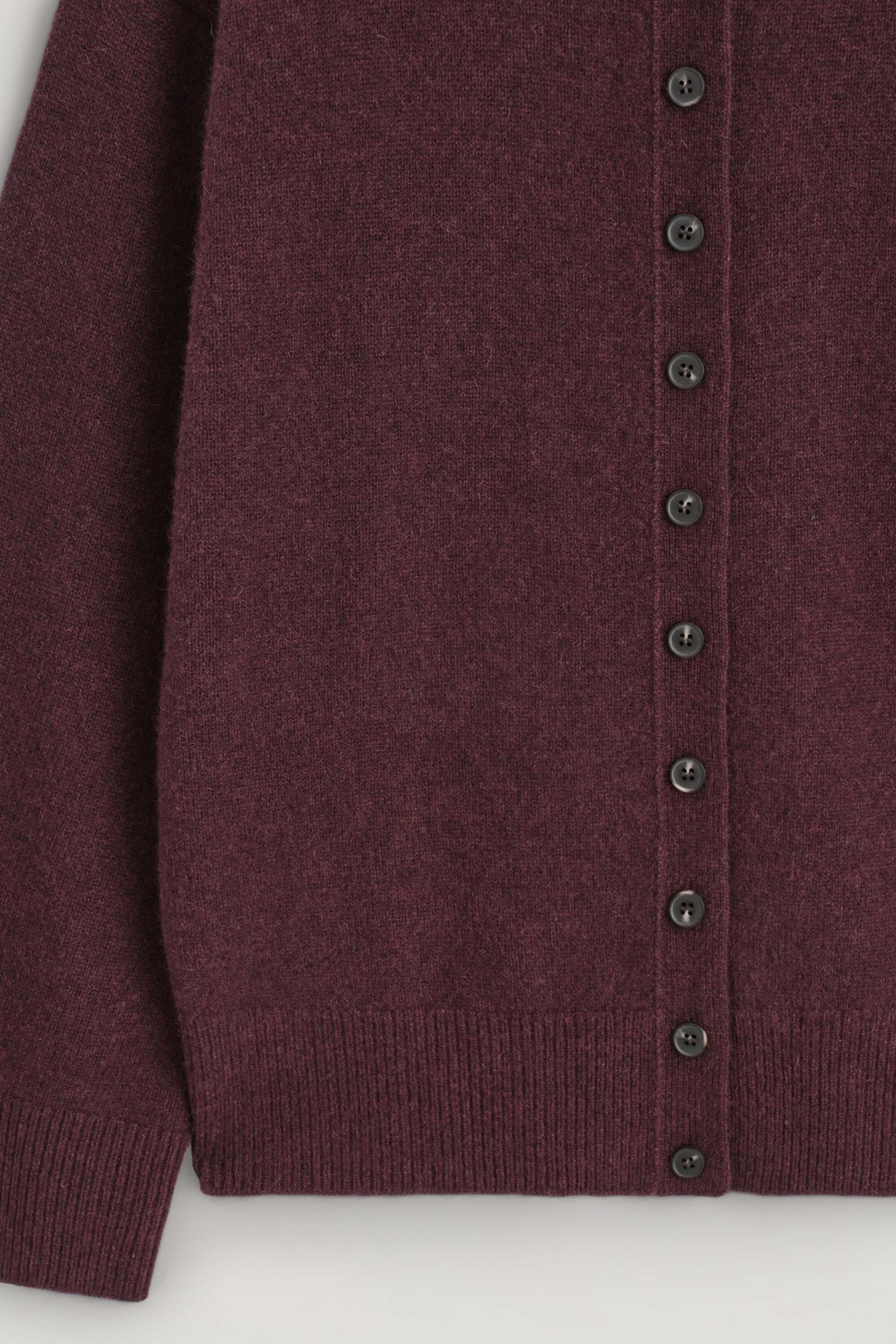 A close-up front view shows a dark burgundy knitted cardigan featuring a vertical button placket with dark round buttons. The cardigan is made from soft-textured knit fabric and features a ribbed hem and ribbed cuff on the sleeve. A close-up front view shows a dark burgundy knitted cardigan featuring a vertical button placket with dark round buttons. The cardigan is made from soft-textured knit fabric and features a ribbed hem and ribbed cuff on the sleeve.
