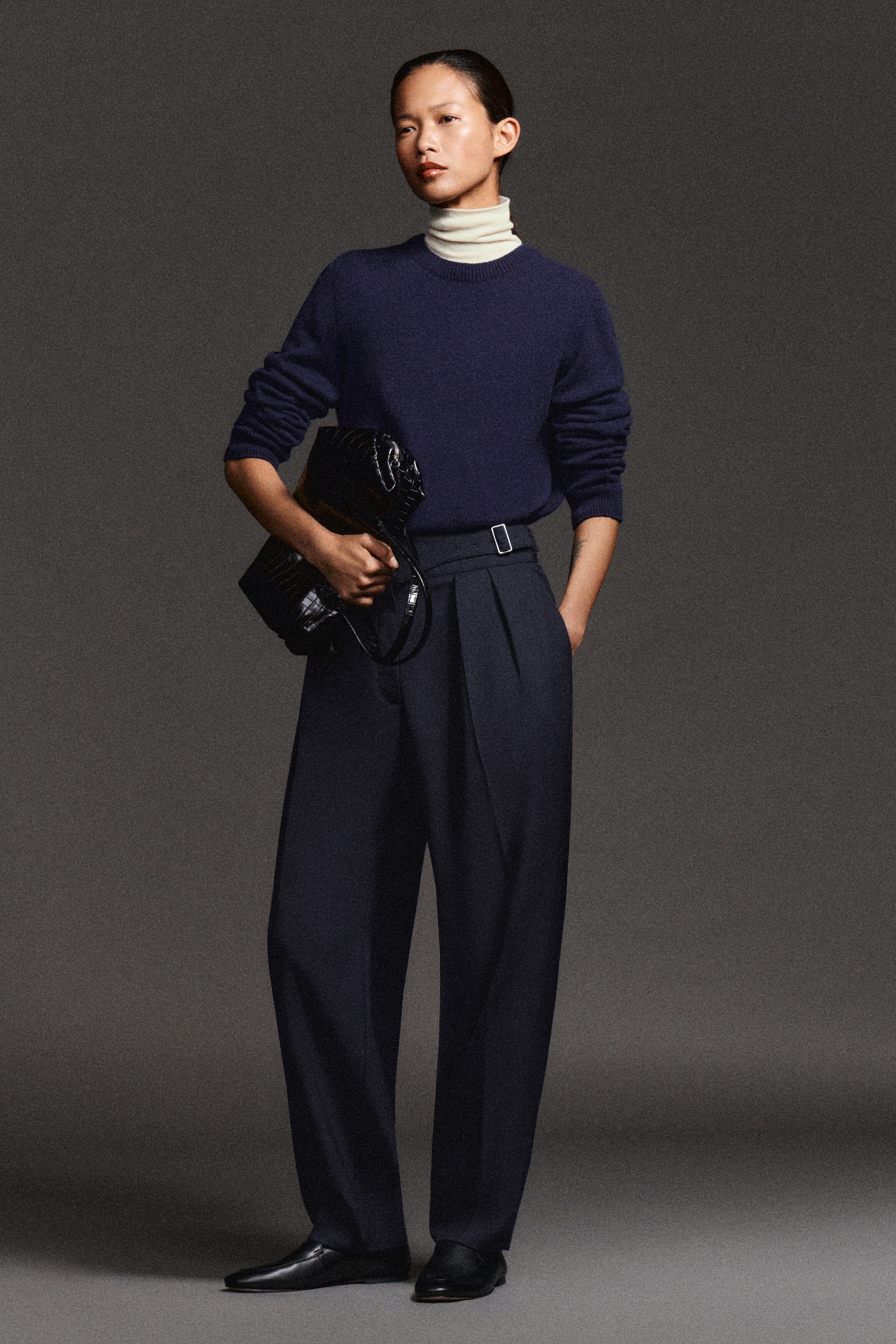 Dark navy barrel-leg trousers, shown from the front, feature a high-rise buckled cummerbund waistband and deep front pleats. A tucked-in navy crew-neck sweater highlights the waist detail, with the trousers tapering slightly at the ankles. Dark navy barrel-leg trousers, shown from the front, feature a high-rise buckled cummerbund waistband and deep front pleats. A tucked-in navy crew-neck sweater highlights the waist detail, with the trousers tapering slightly at the ankles.