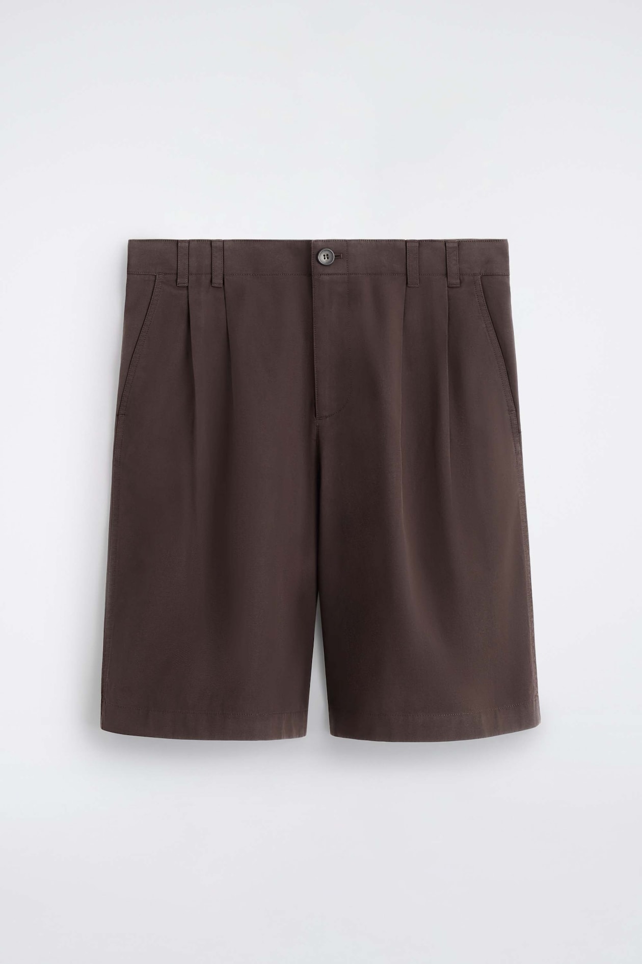 These dark brown tailored pleated cotton shorts are shown from the front, featuring a structured waistband with belt loops, a single-button fastening, double front pleats, and side slant pockets.