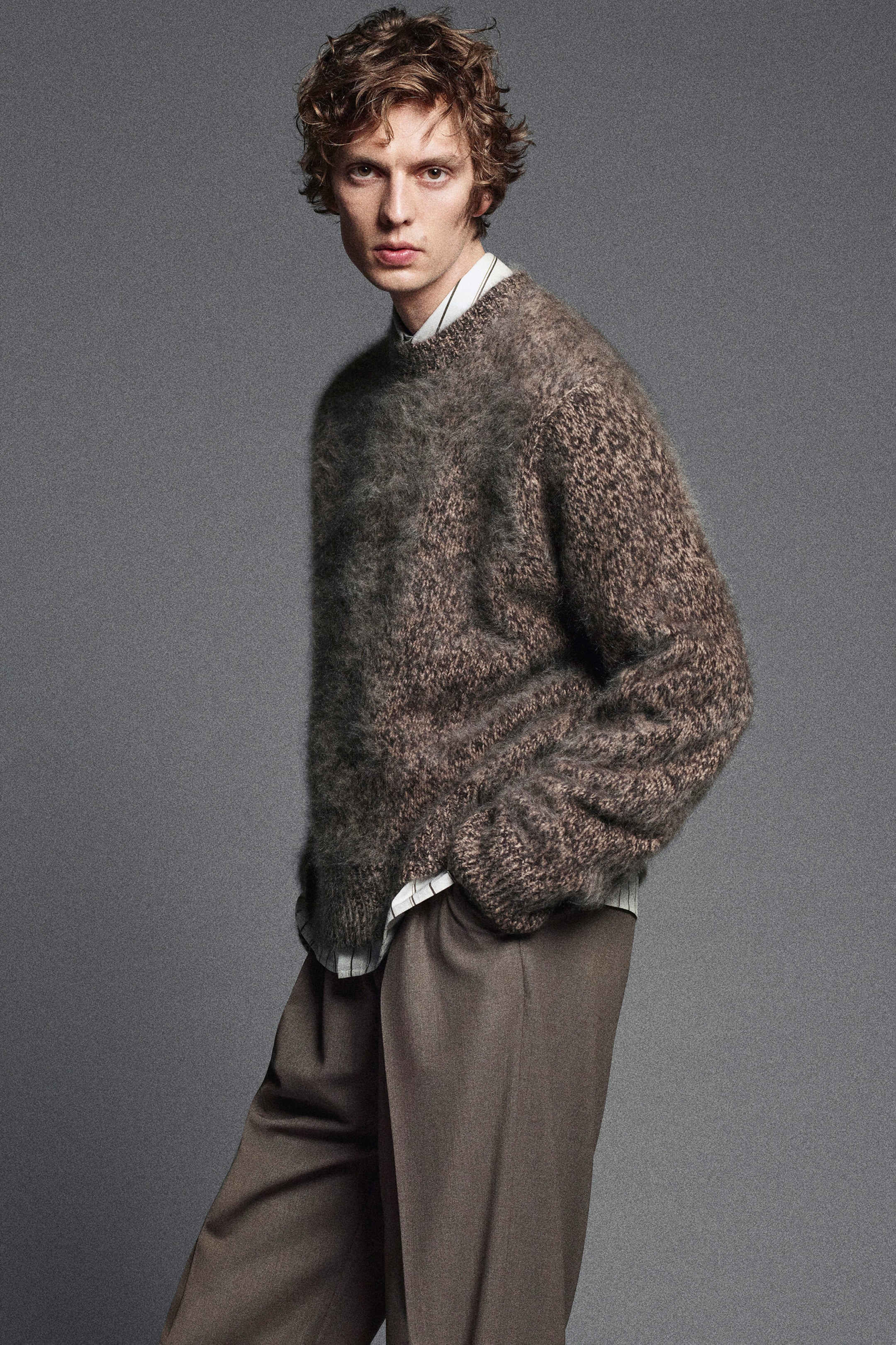 The two-tone brushed-cashmere crew-neck jumper is shown from a three-quarter front angle, highlighting its fuzzy, highly textured knit in blended brown and grey tones. The relaxed-fit garment features ribbed trims at the collar, cuffs, and hem, and is layered over a striped collared shirt. The two-tone brushed-cashmere crew-neck jumper is shown from a three-quarter front angle, highlighting its fuzzy, highly textured knit in blended brown and grey tones. The relaxed-fit garment features ribbed trims at the collar, cuffs, and hem, and is layered over a striped collared shirt.