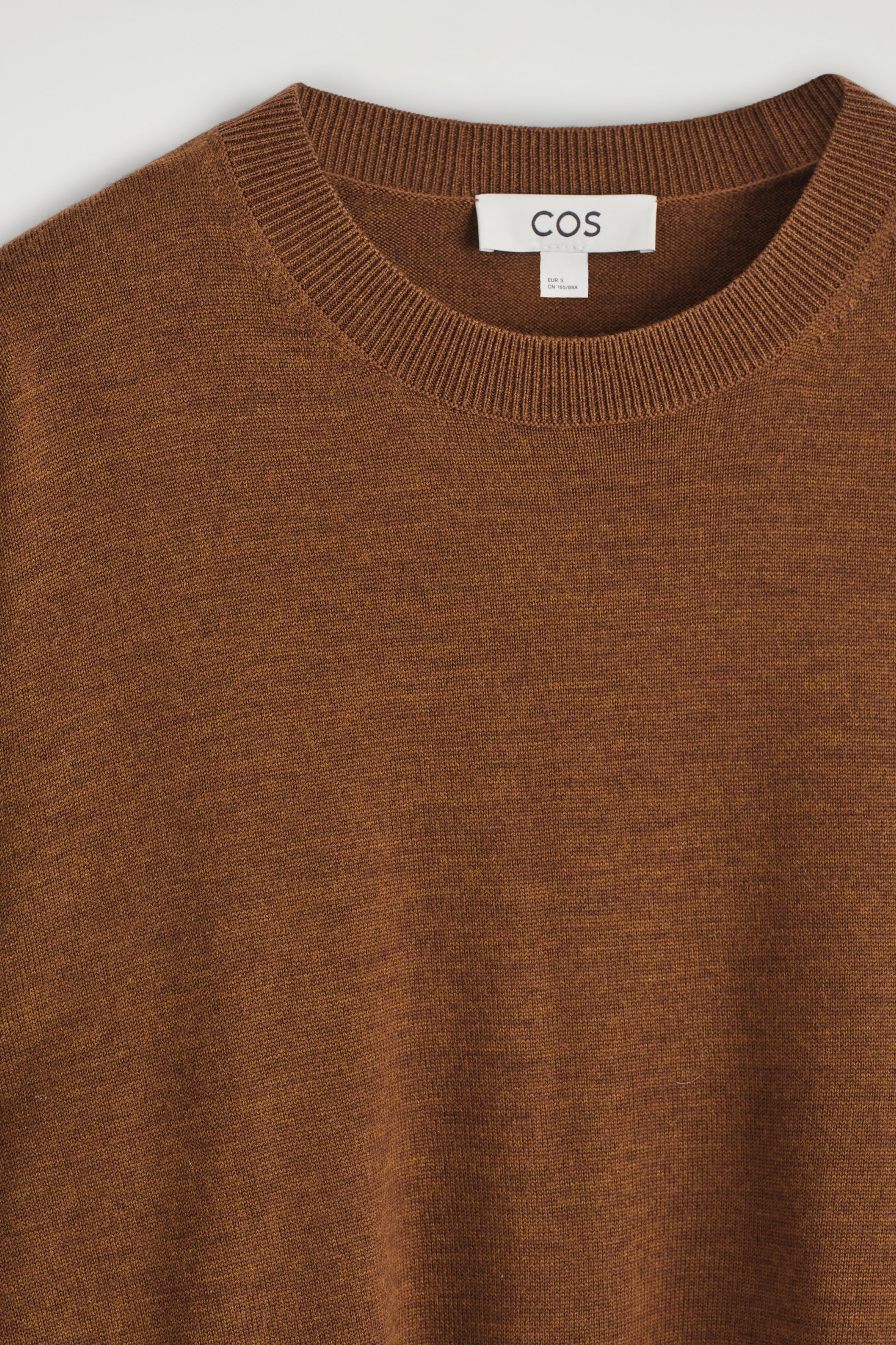 Agrandir l'image: Un pull en mélange brun est présenté de face, avec une texture finement tricotée et un col rond côtelé. Une étiquette de marque 'COS' blanche est visible à l'arrière du cou.