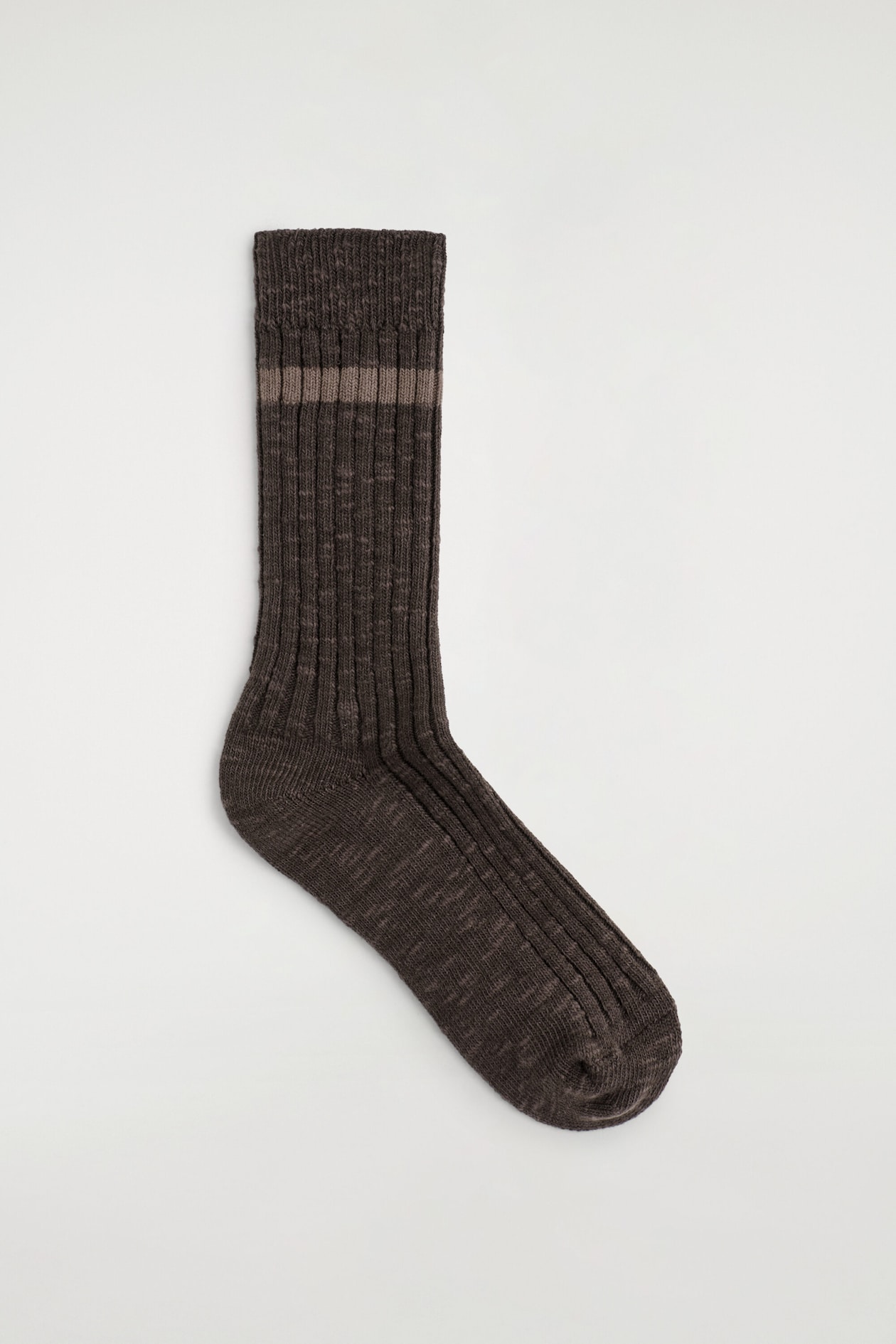 Une seule chaussette mi-mollet en tricot brun foncé chiné est posée à plat, mettant en valeur son profil latéral. Elle présente une texture côtelée le long de la jambe et du dessus du pied, une bordure côtelée unie et une seule bande horizontale brun clair près du haut.