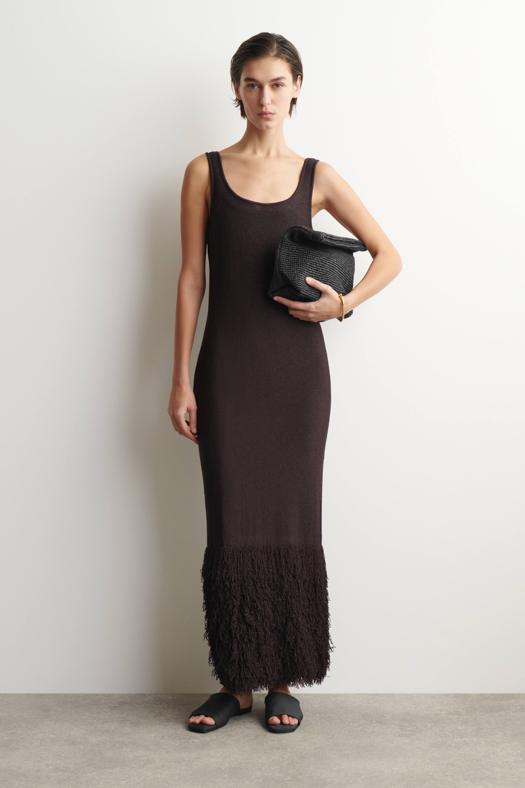 Agrandir l'image: Une robe maxi en maille texturée brun foncé est présentée de face, avec un col rond, de larges bretelles, une silhouette ajustée et un ourlet effiloché et frangé.