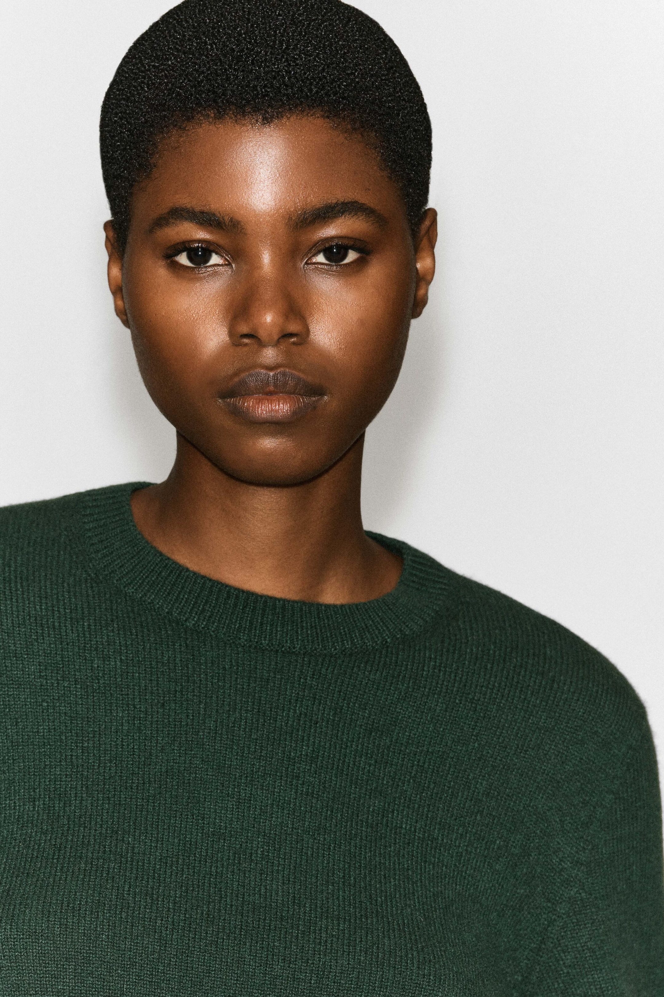 A dark green cashmere crew-neck sweater with a ribbed neckline and a fine-knit texture is being worn by the model. A dark green cashmere crew-neck sweater with a ribbed neckline and a fine-knit texture is being worn by the model.