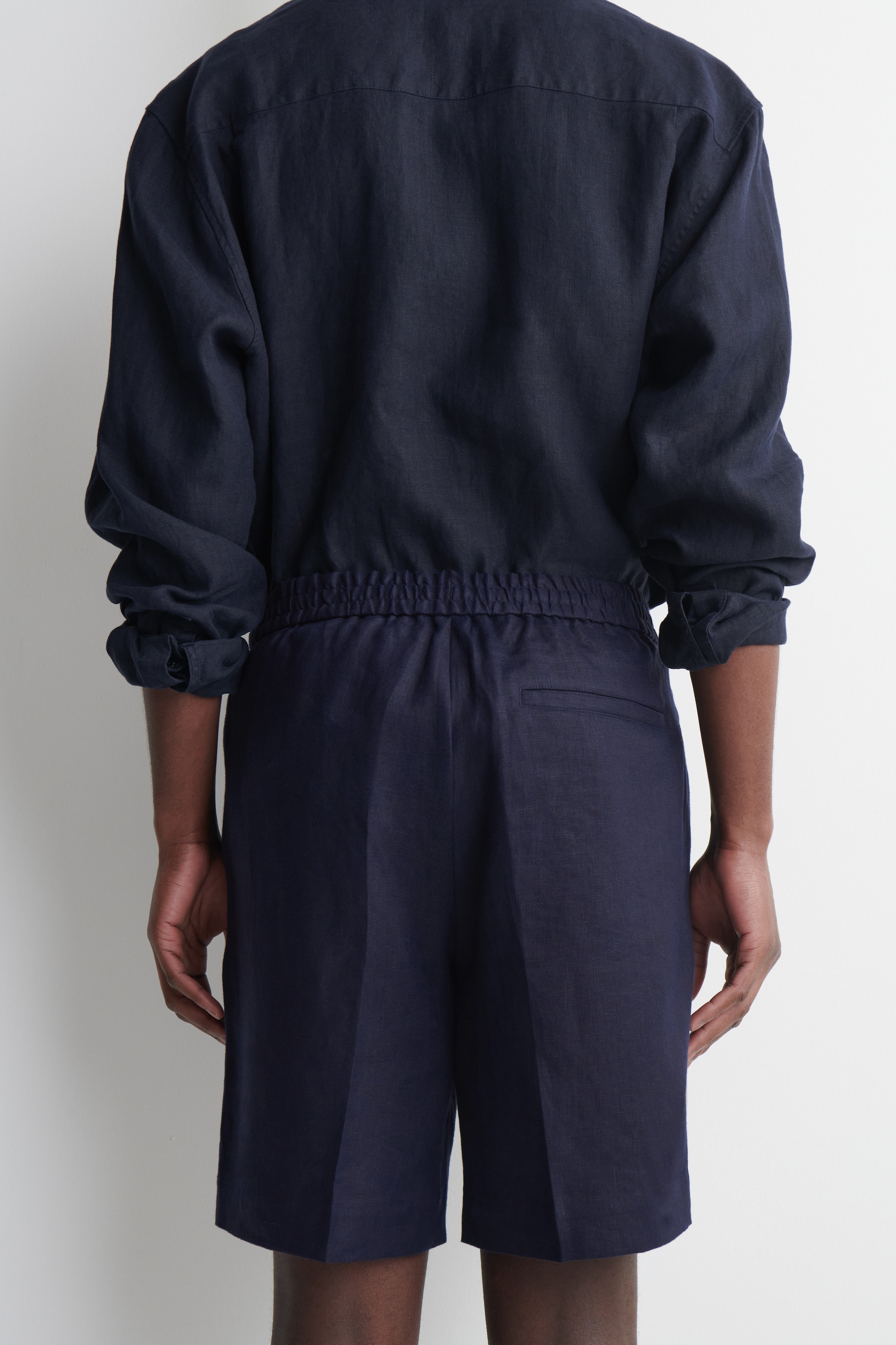 Visualizza immagine più grande: Una camicia a maniche lunghe blu navy, vista da dietro, mostra un orlo arricciato elasticizzato e maniche arrotolate, mentre i pantaloncini blu navy coordinati presentano una cintura elasticizzata e una tasca posteriore a filetto.