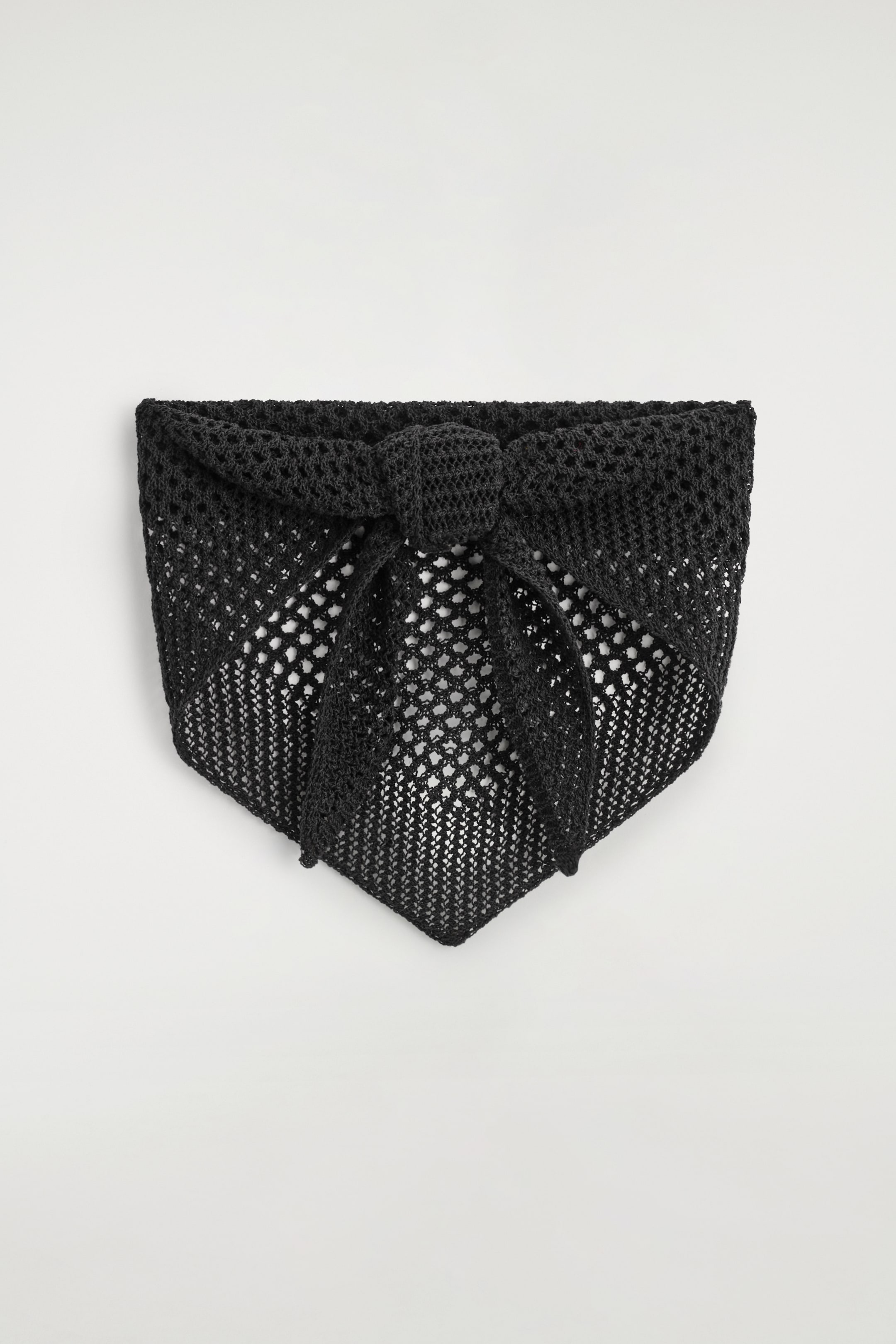 View larger image: The black triangle scarf is presenting its front, featuring an openwork pointelle knit pattern throughout. A knot is tied at the top center of the scarf.